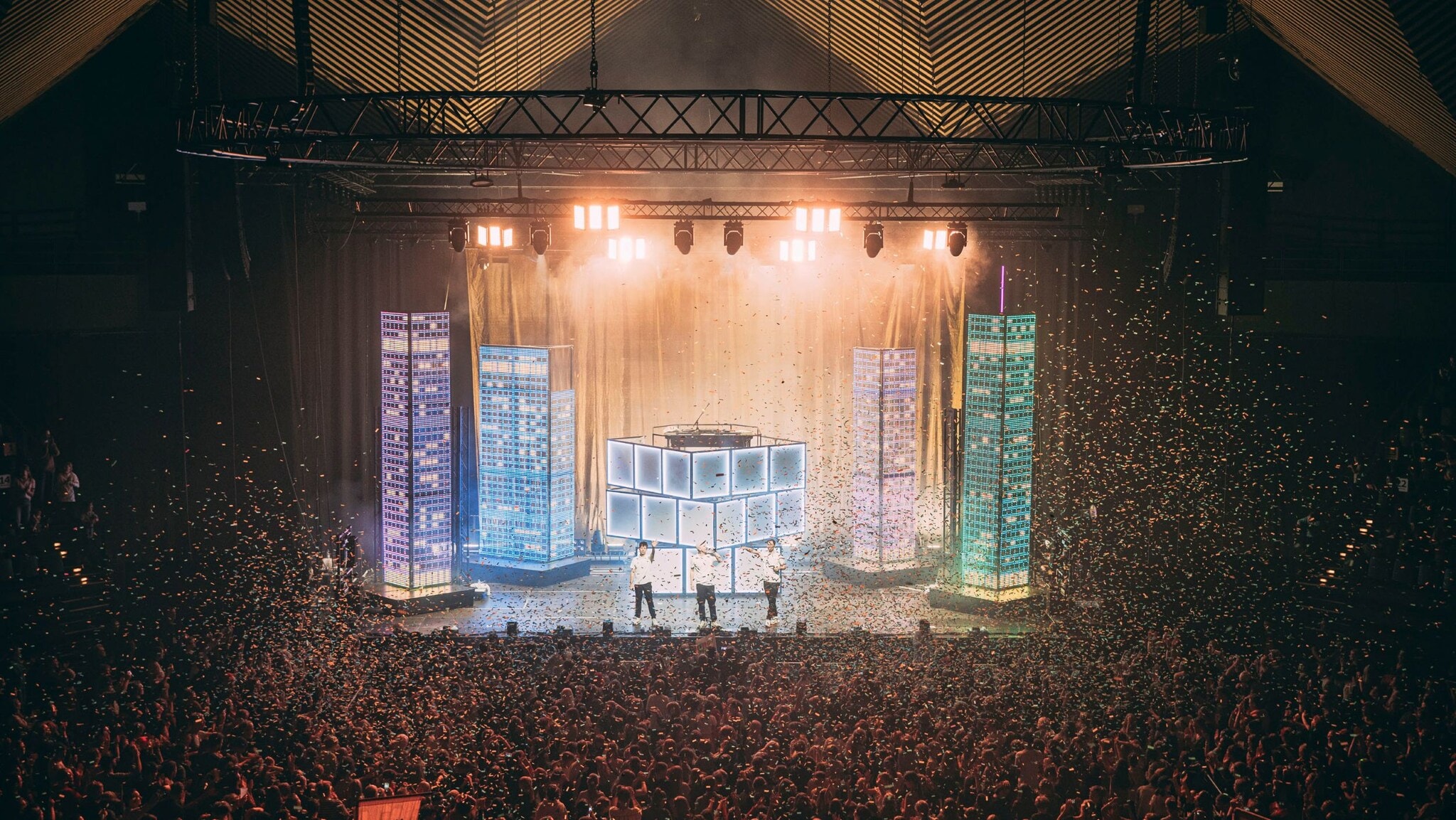 Große Menschenmenge bei einem Konzert oder Event in einer Halle mit beleuchtetem Bühnenbereich und Nebeleffekten. Große Menschenmenge bei einem Konzert oder Event in einer Halle mit beleuchtetem Bühnenbereich und Nebeleffekten.