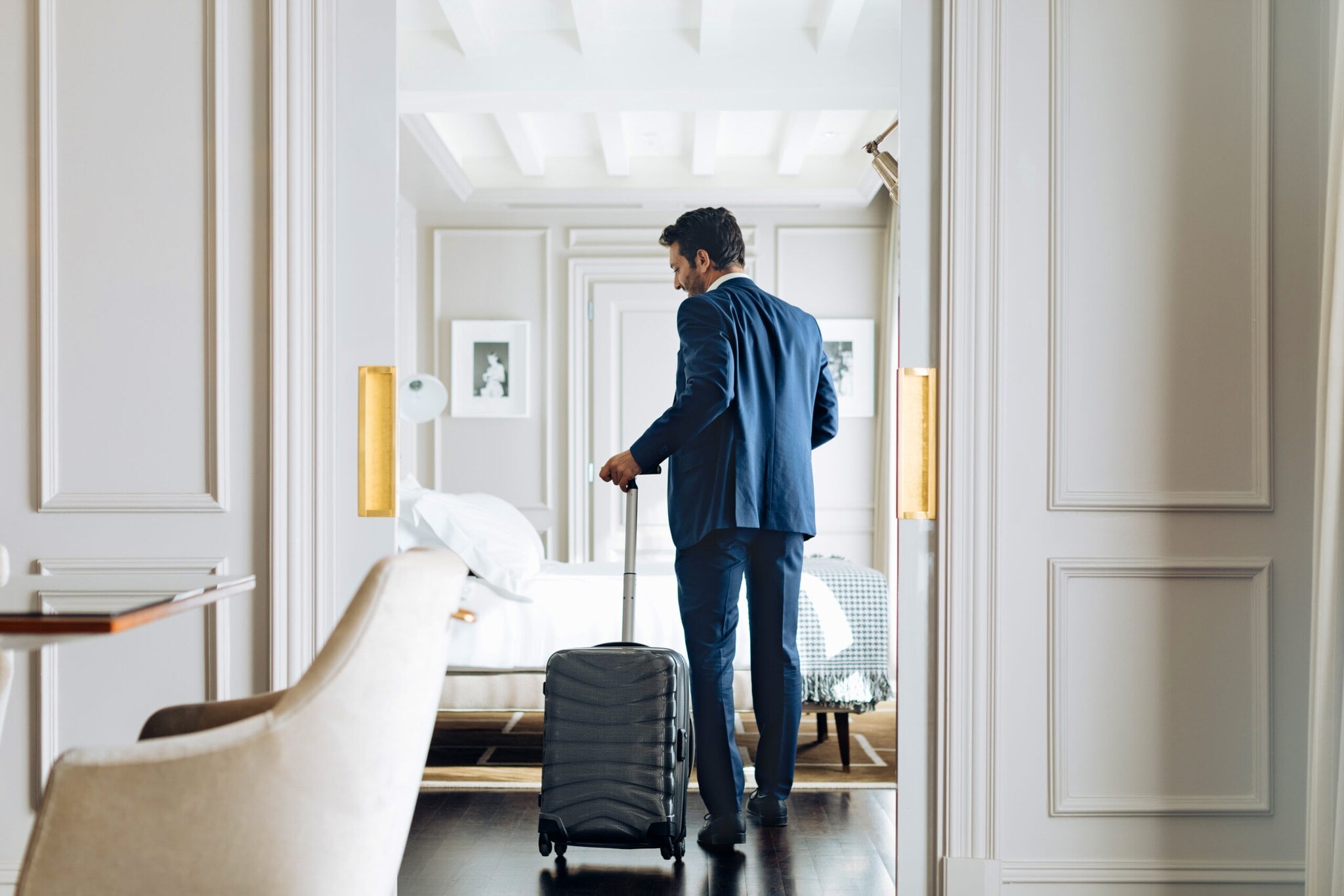 Mann im Anzug und einem Rollkoffer in der Hand betritt eine helle luxuriöse Hotel-Suite. Mann im Anzug und einem Rollkoffer in der Hand betritt eine helle luxuriöse Hotel-Suite.