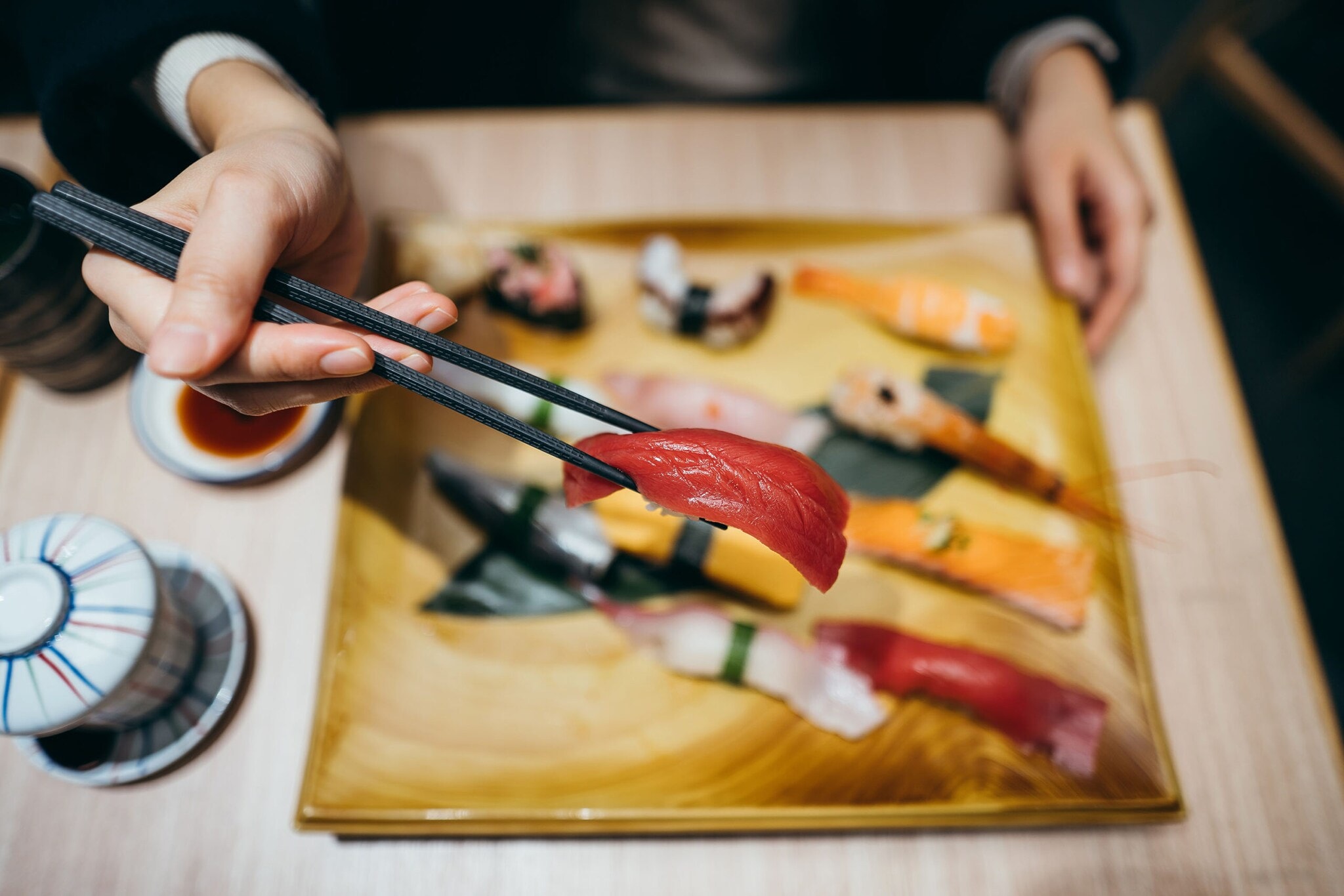 Eine Hand mit Stäbchen über einem Teller mit verschiedenen Sushi-Sorten. Eine Hand mit Stäbchen über einem Teller mit verschiedenen Sushi-Sorten.