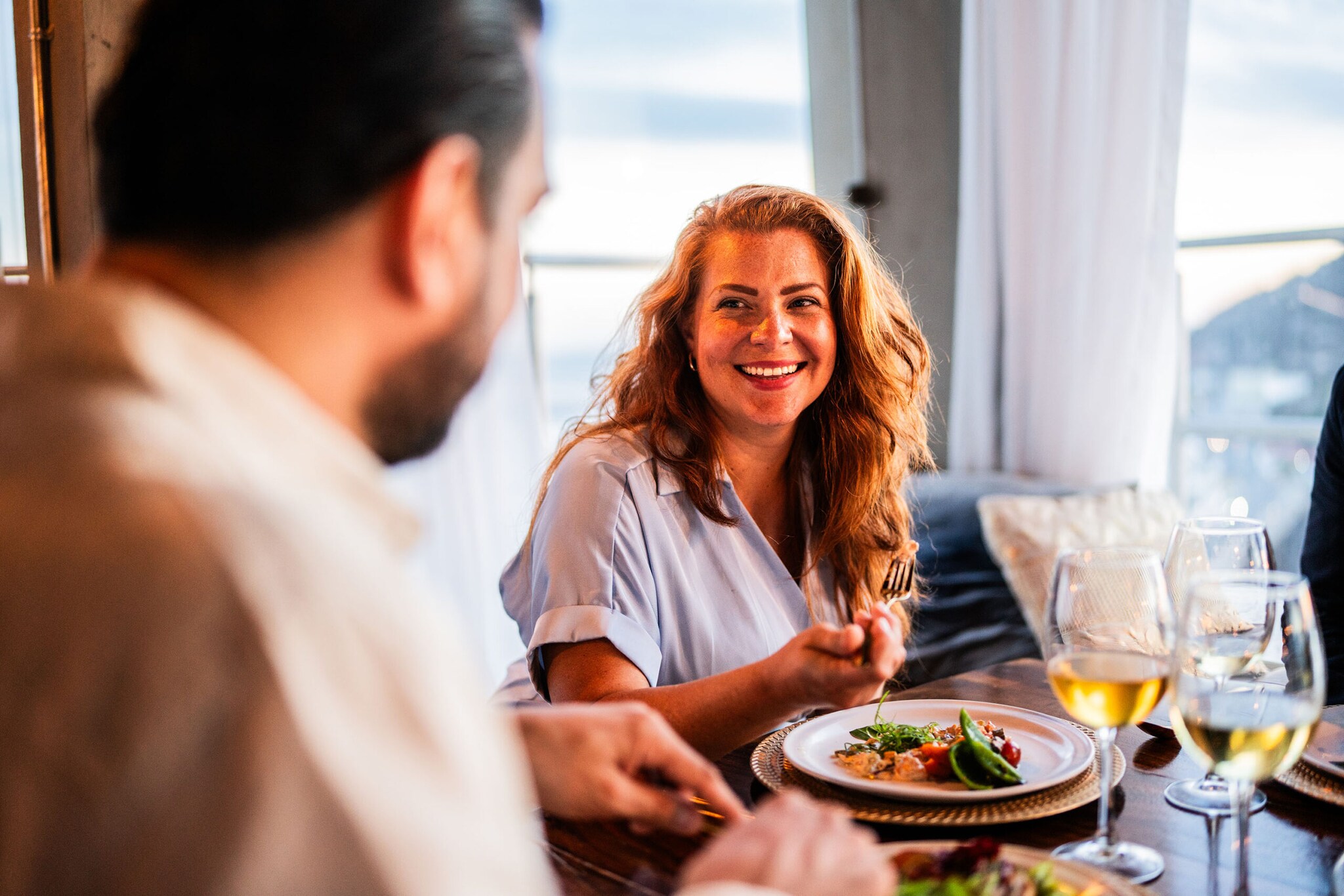 Eine lächelnde Frau im Restaurant sitzt einem Mann gegenüber, zwischen ihnen steht ein hübsch angerichteter Teller.