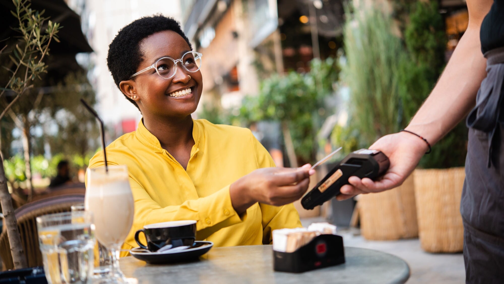 Eine lächelnde Frau bezahlt kontaktlos mit einer Kreditkarte an einem Kartenlesegerät an einem Tisch in der Außengastronomie. Eine lächelnde Frau bezahlt kontaktlos mit einer Kreditkarte an einem Kartenlesegerät an einem Tisch in der Außengastronomie.