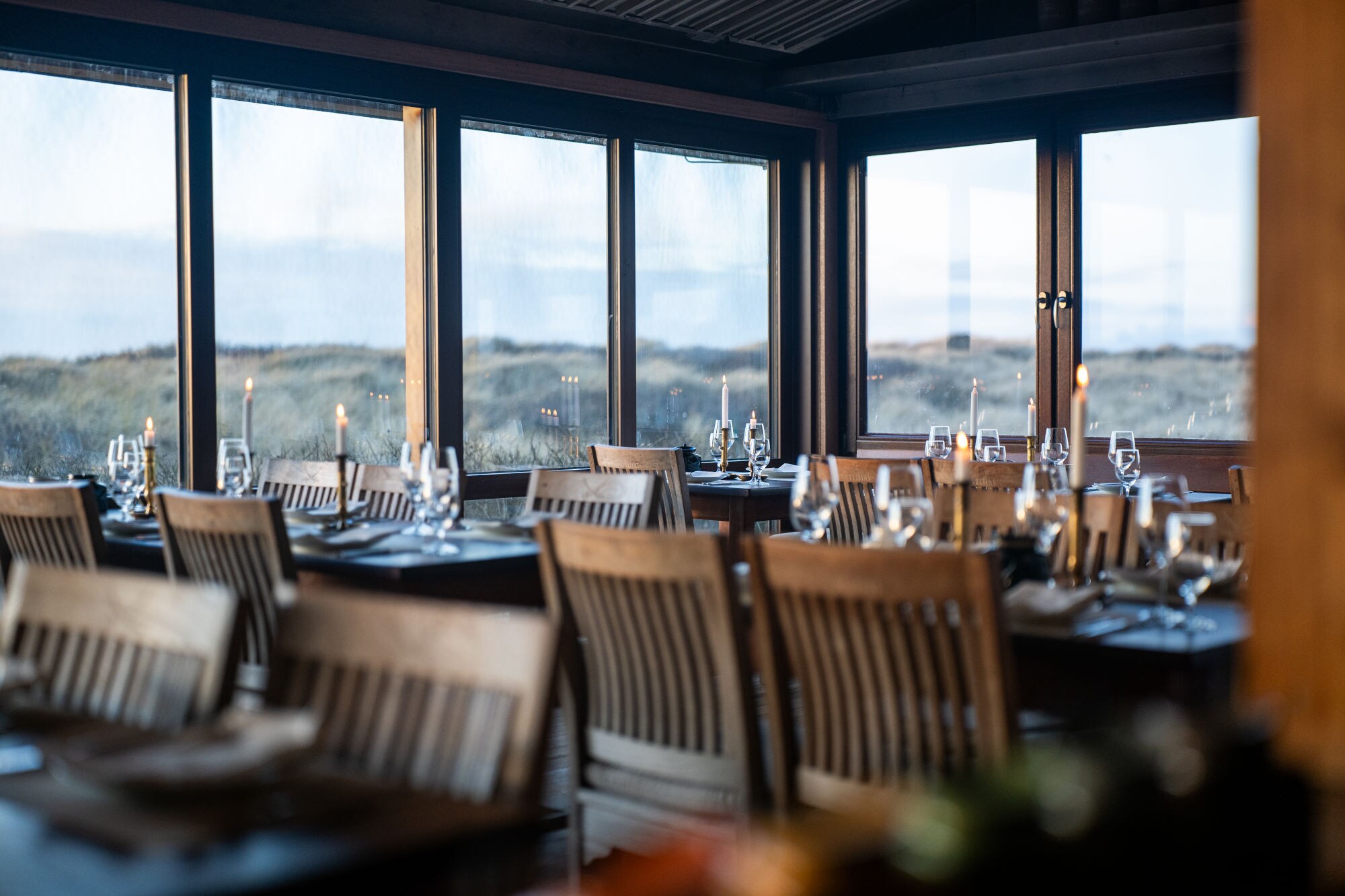 Gastraum der Sylter Sansibar, mit eleganten Tischen und Stühlen aus dunklem Holz und einem herrlichen Ausblick auf die umliegende Dünenlandschaft.