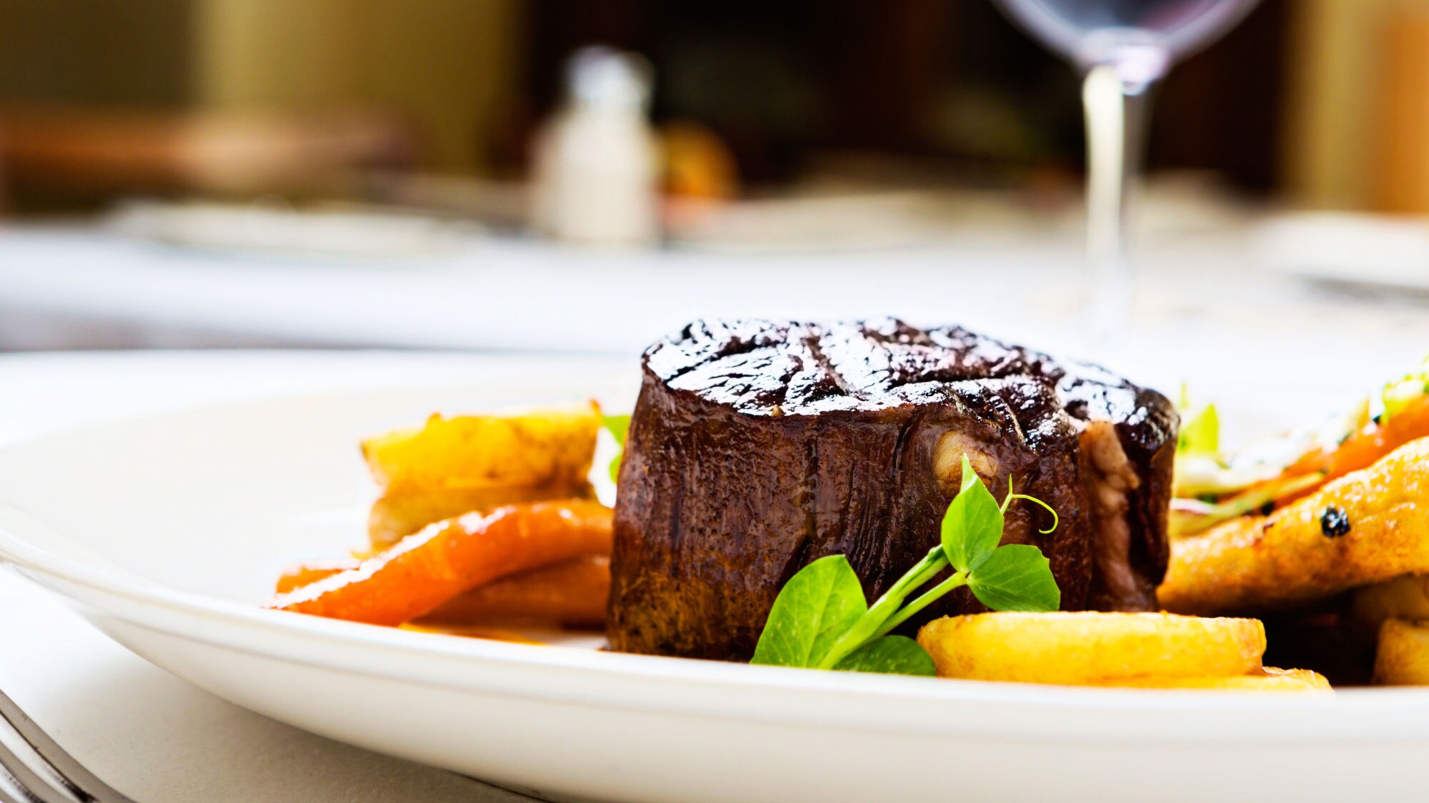 Gegrilltes Rinderfilet auf weißem Teller mit gebratenen Karotten und grünen Erbsensprossen.