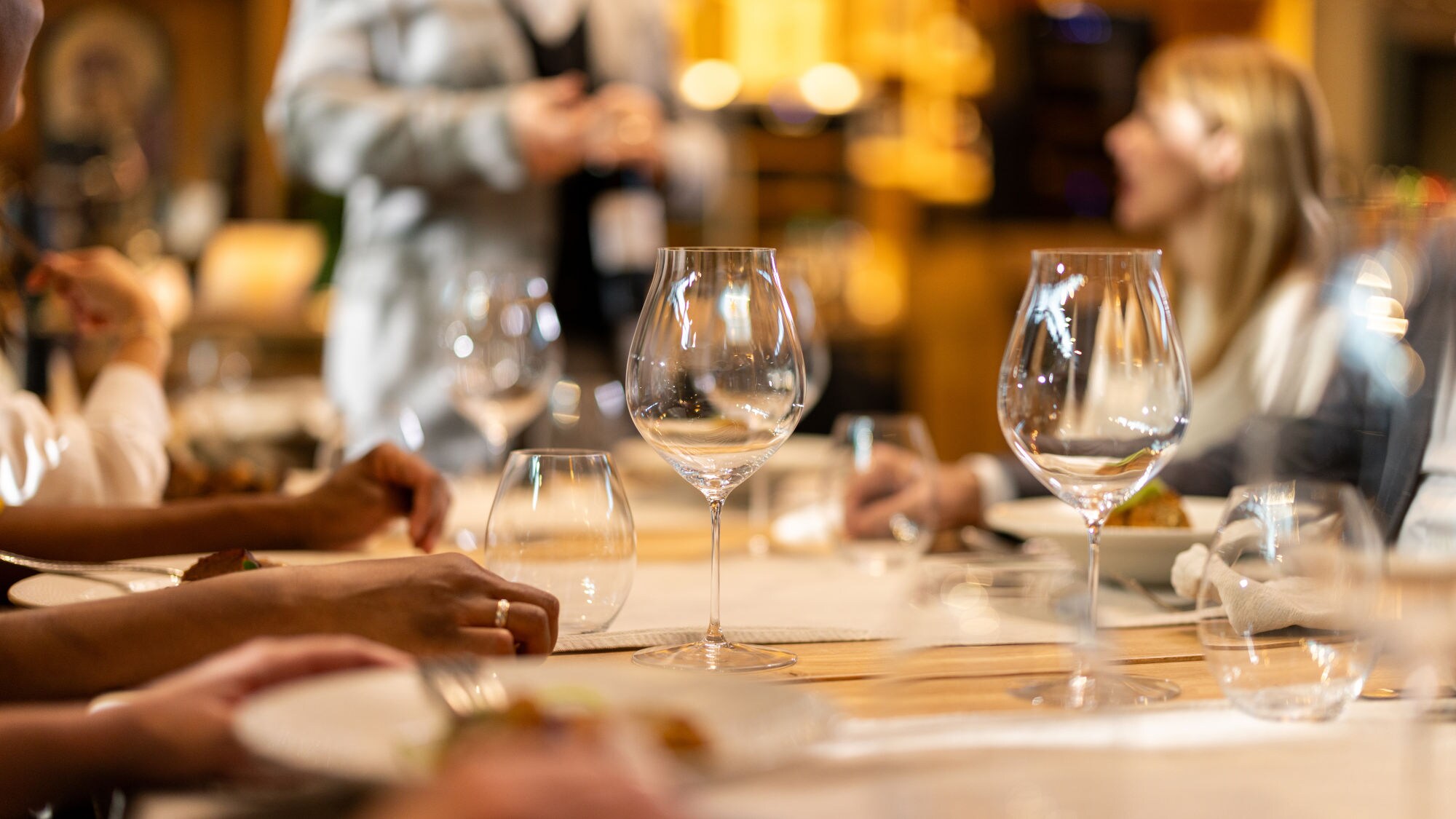 Weingläser auf einem gedeckten Holztisch in einem Restaurant mit Menschen im Hintergrund.