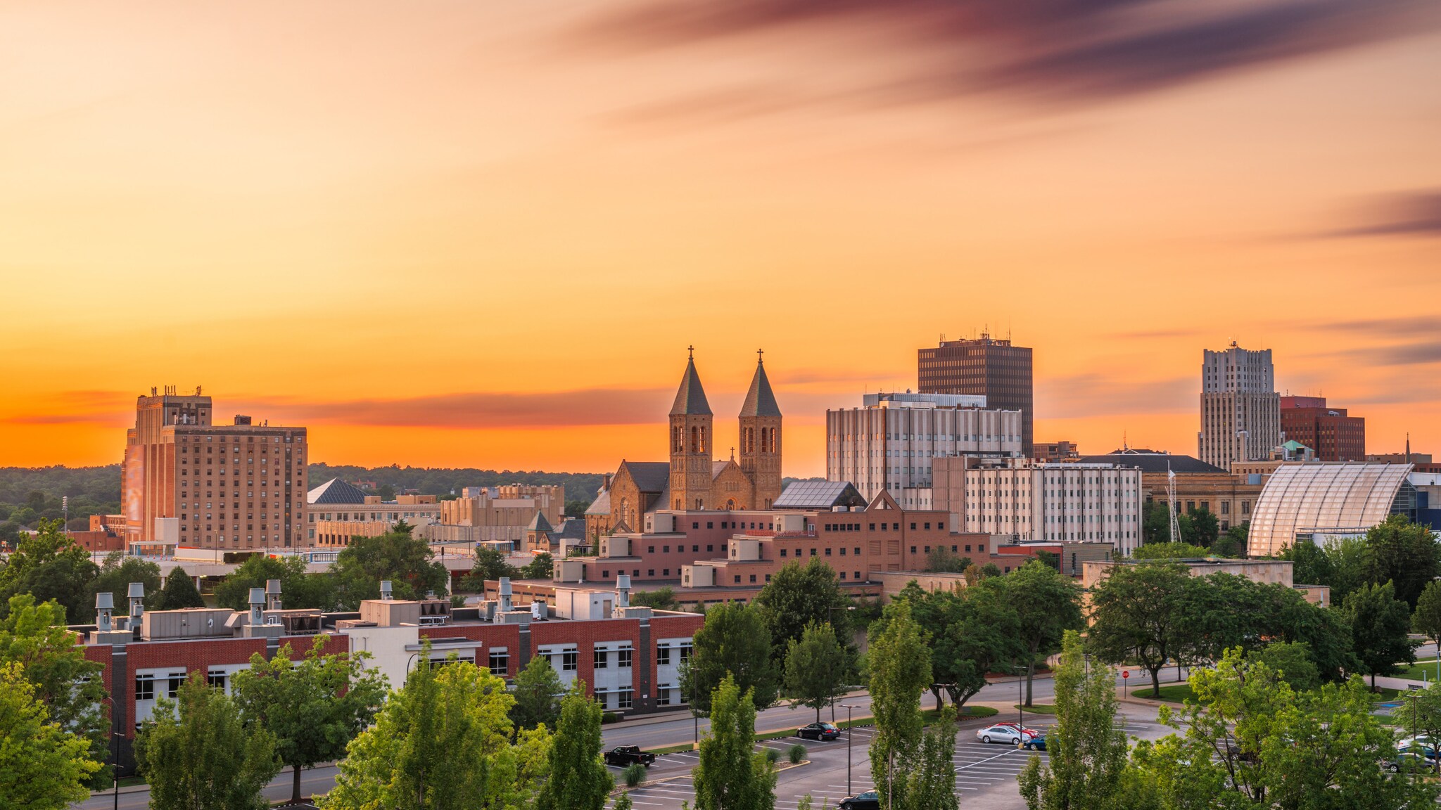 Stadtansicht von Akron bei Sonnenuntergang mit Gebäuden, zwei Kirchtürmen und Bäumen im Vordergrund Stadtansicht von Akron bei Sonnenuntergang mit Gebäuden, zwei Kirchtürmen und Bäumen im Vordergrund