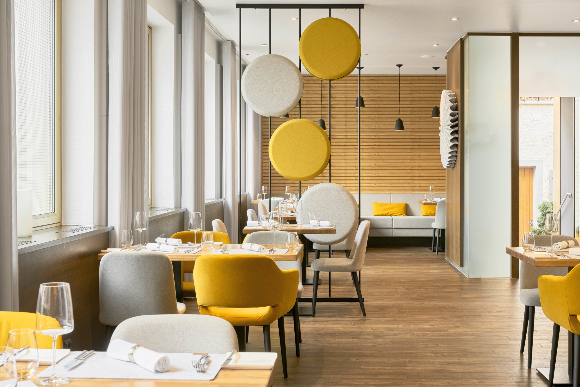 Helles stilvolles Interieur mit gelben und cremefarbenen Sitzmöbeln, dekorativer Trennwand und holzverkleideten Wänden.