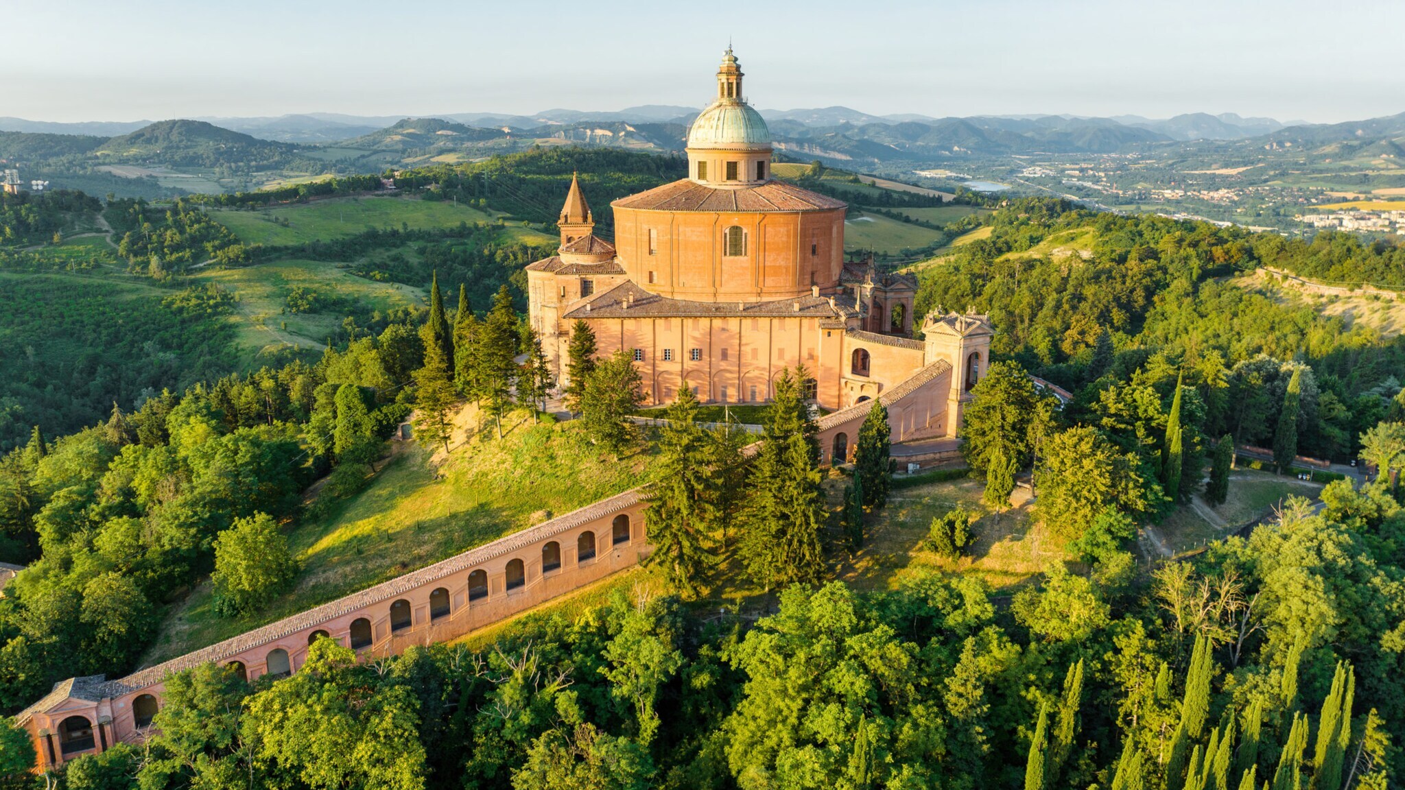 Historische Kuppelkirche auf einem bewaldeten Hügel mit umliegender Landschaft und Bergen im Hintergrund