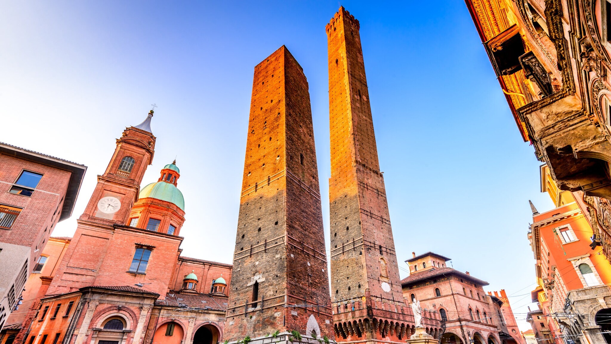 Zwei mittelalterliche schiefe Türme in Bologna, Italien, umgeben von historischen Gebäuden bei klarem Himmel