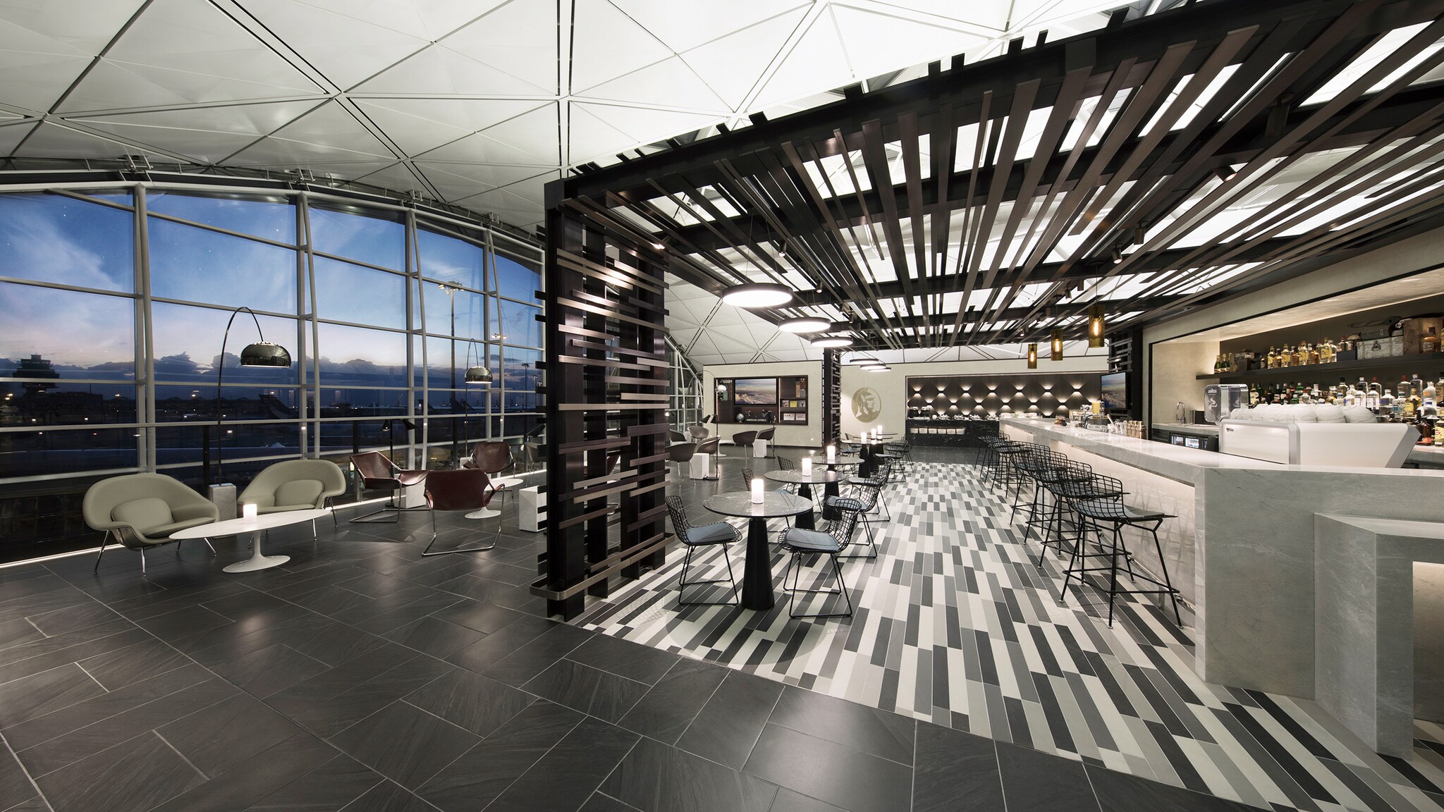 Menschenleere, moderne Flughafenlounge mit Barbereich und Panoramablick aufs Rollfeld am Abend.