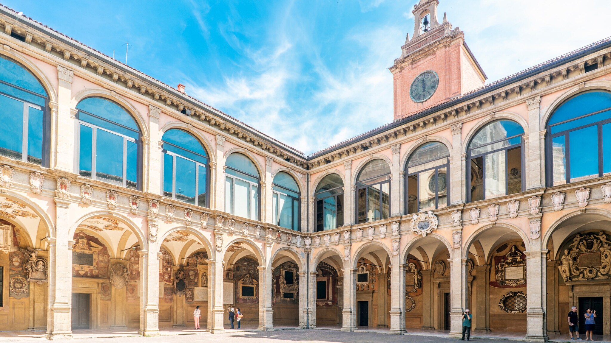 Innenhof eines historischen Gebäudes mit Arkadengängen, verzierten Säulen und einem Uhrturm unter blauem Himmel