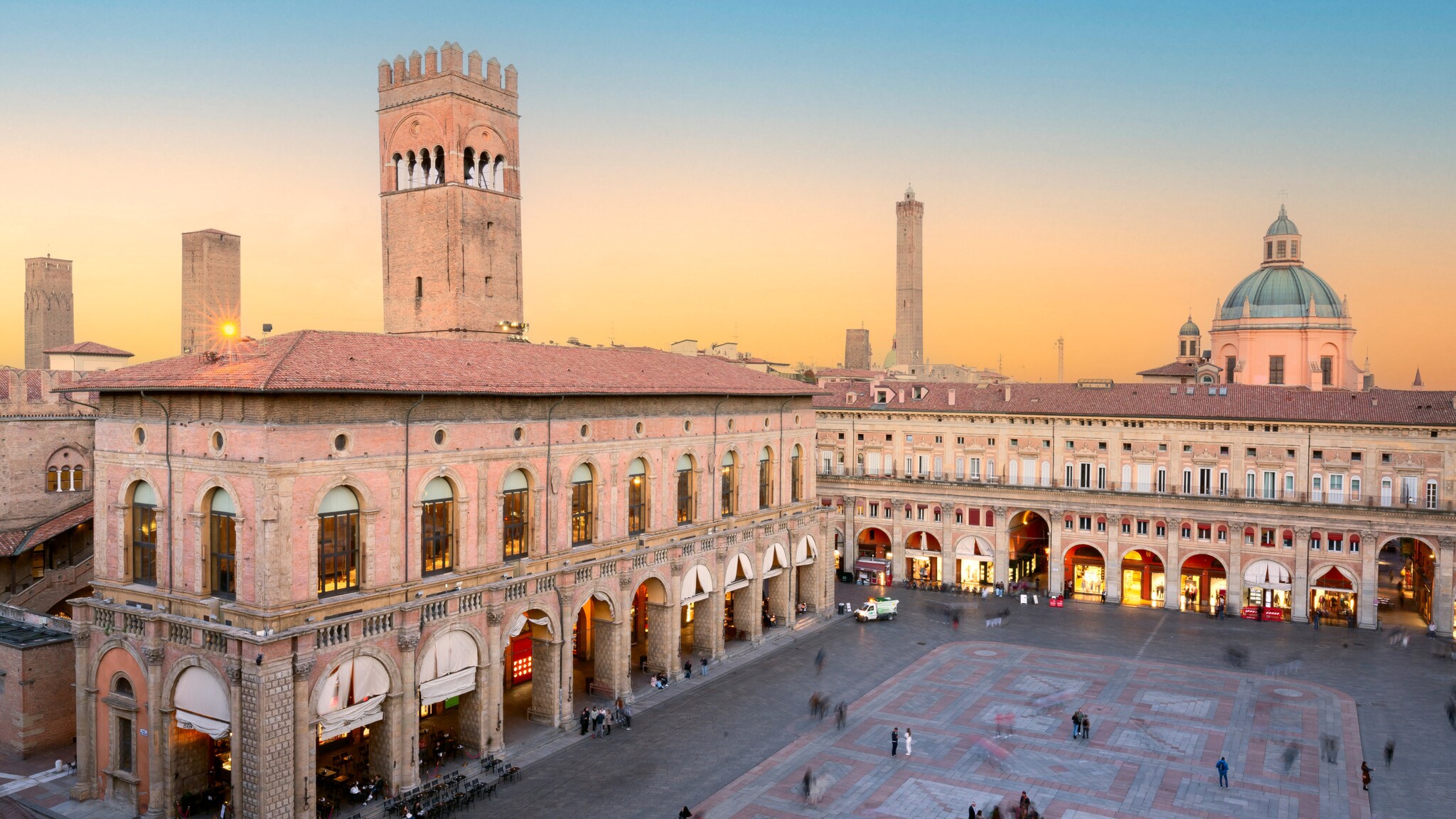 Historische Gebäude mit Arkaden und Turm am Piazza Maggiore in Bologna bei Sonnenuntergang