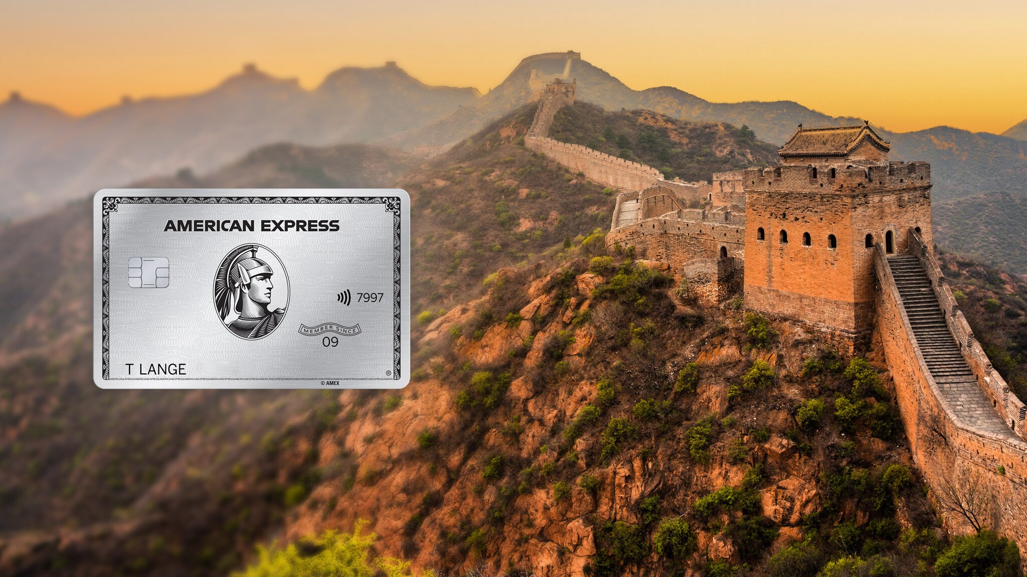 Abschnitt der Chinesischen Mauer mit Wachturm in Berglandschaft bei Sonnenuntergang, im Vordergrund eine silberne Platinum Kreditkarte von American Express als Freisteller. Abschnitt der Chinesischen Mauer mit Wachturm in Berglandschaft bei Sonnenuntergang, im Vordergrund eine silberne Platinum Kreditkarte von American Express als Freisteller.