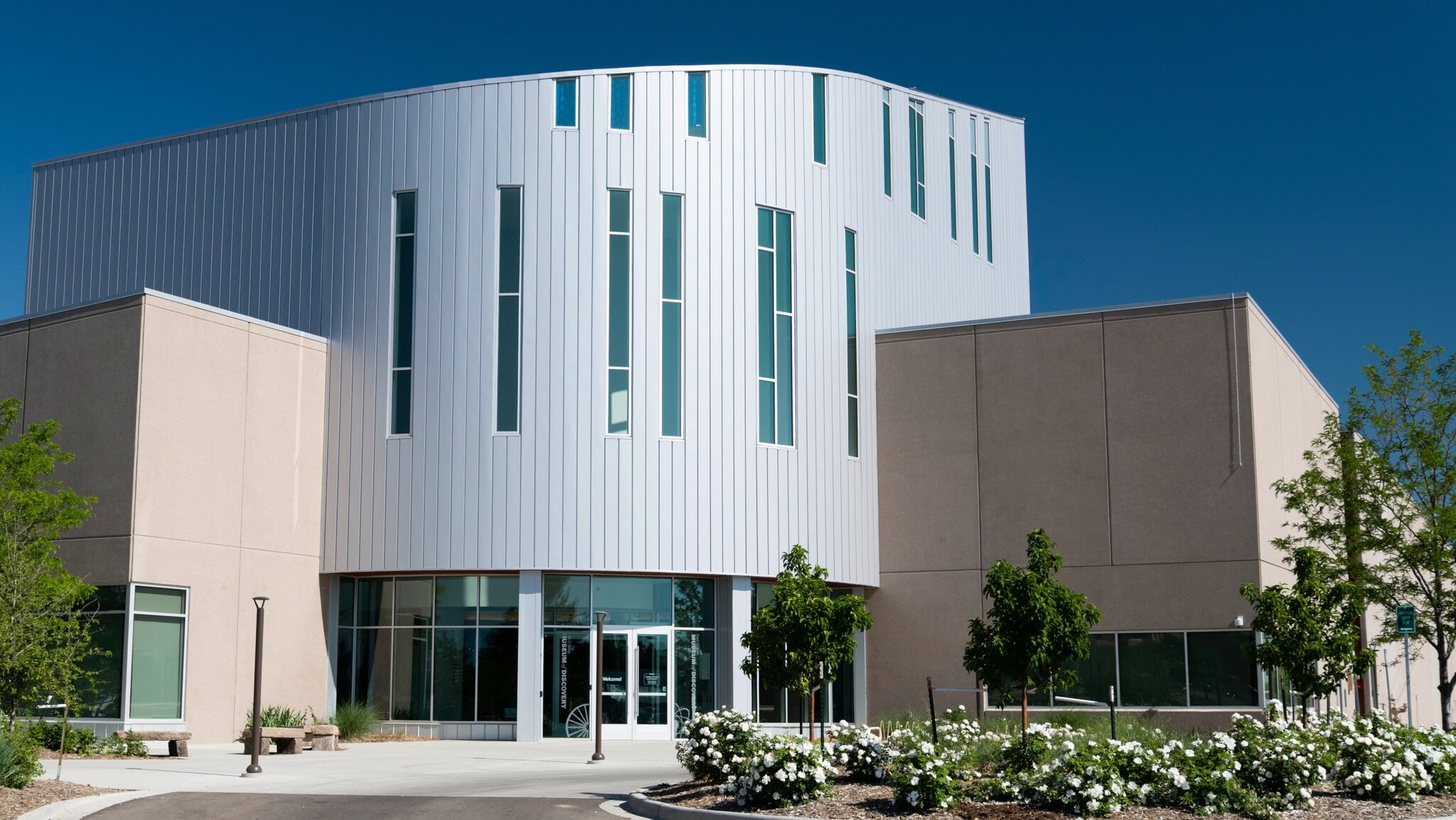 Modernes Gebäude mit weißer Fassade, großen Fenstern und rundem Eingang unter klarem blauem Himmel Modernes Gebäude mit weißer Fassade, großen Fenstern und rundem Eingang unter klarem blauem Himmel