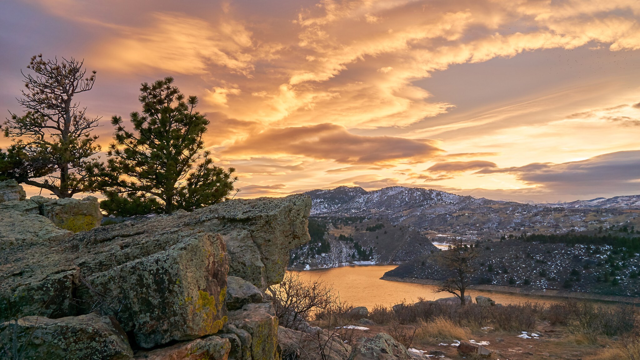 Felsige Landschaft mit Nadelbäumen und See bei Sonnenuntergang unter bewölktem Himmel Felsige Landschaft mit Nadelbäumen und See bei Sonnenuntergang unter bewölktem Himmel