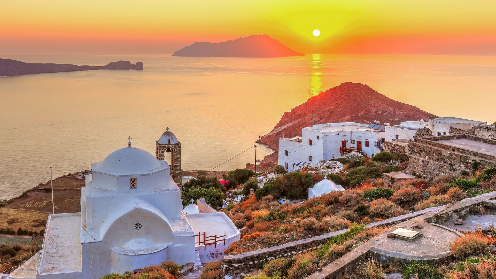 Blick aufs Meer bei Sonnenuntergang von einer Festung mit einer kleinen Kirche auf einem Hügel mit weiß getünchten Häusern.