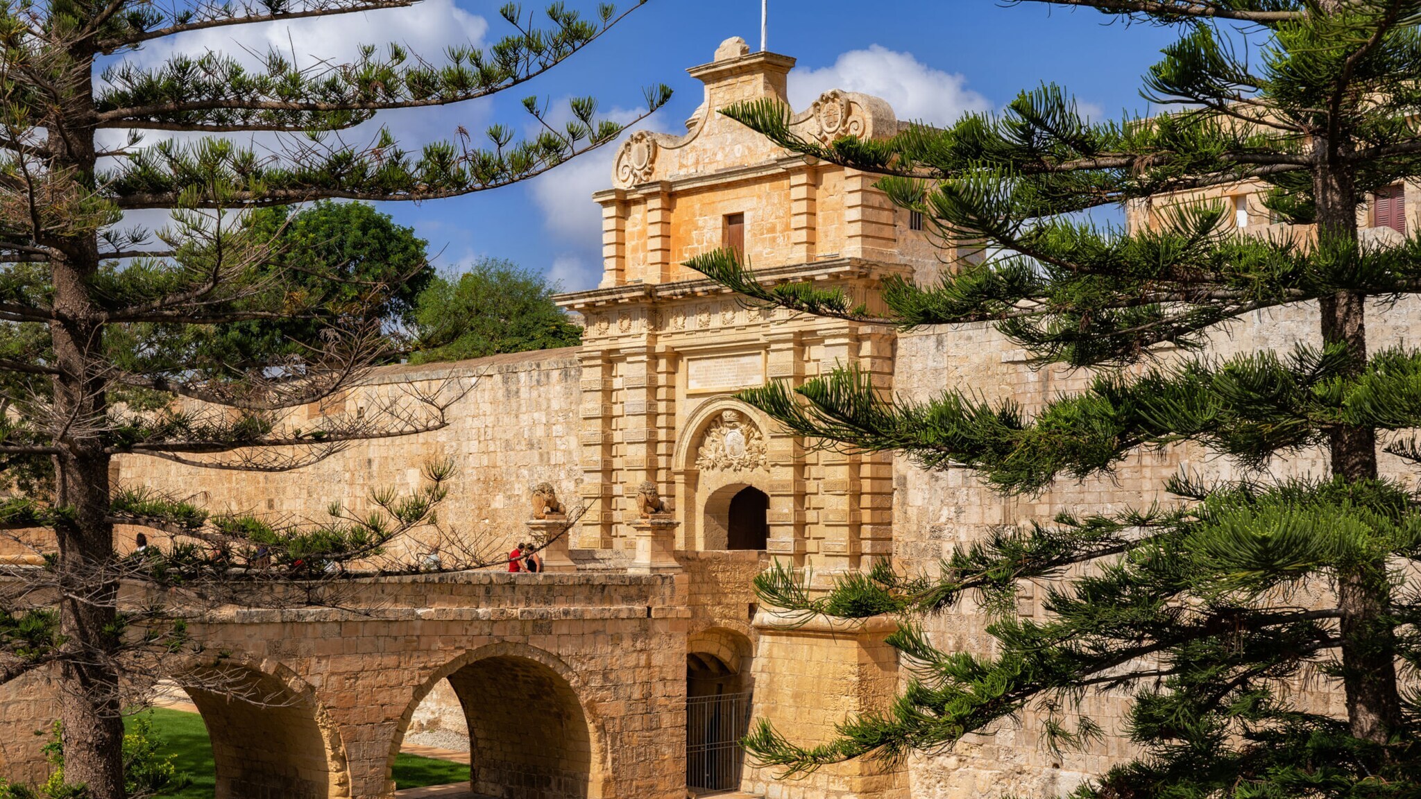 Historisches Tor mit Brücke und Steinbögen, umgeben von grünen Bäumen unter blauem Himmel. Historisches Tor mit Brücke und Steinbögen, umgeben von grünen Bäumen unter blauem Himmel.