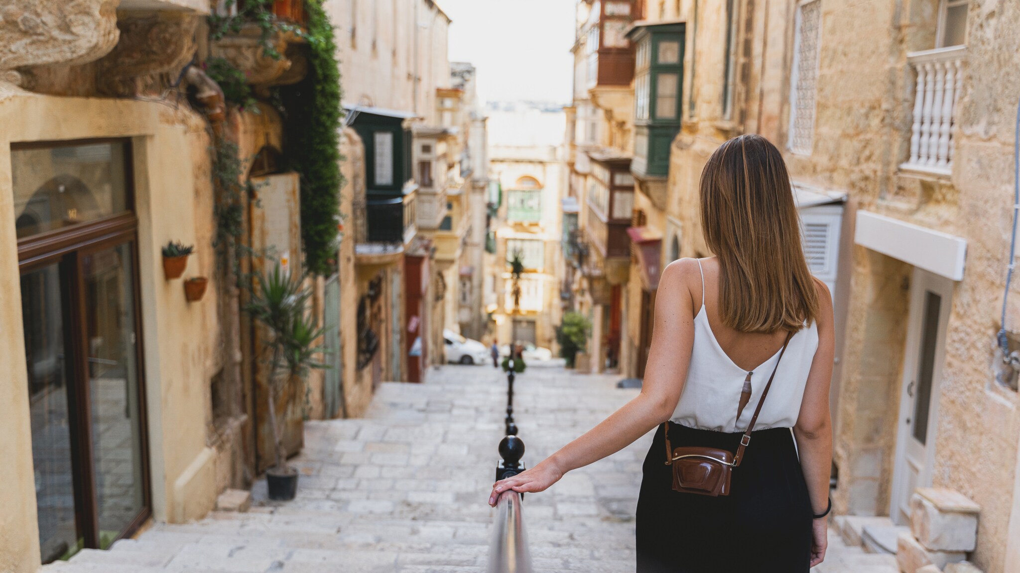 Frau mit weißem Top und schwarzer Hose geht eine steinerne Treppe in einer engen Gasse mit historischen Gebäuden hinunter Frau mit weißem Top und schwarzer Hose geht eine steinerne Treppe in einer engen Gasse mit historischen Gebäuden hinunter