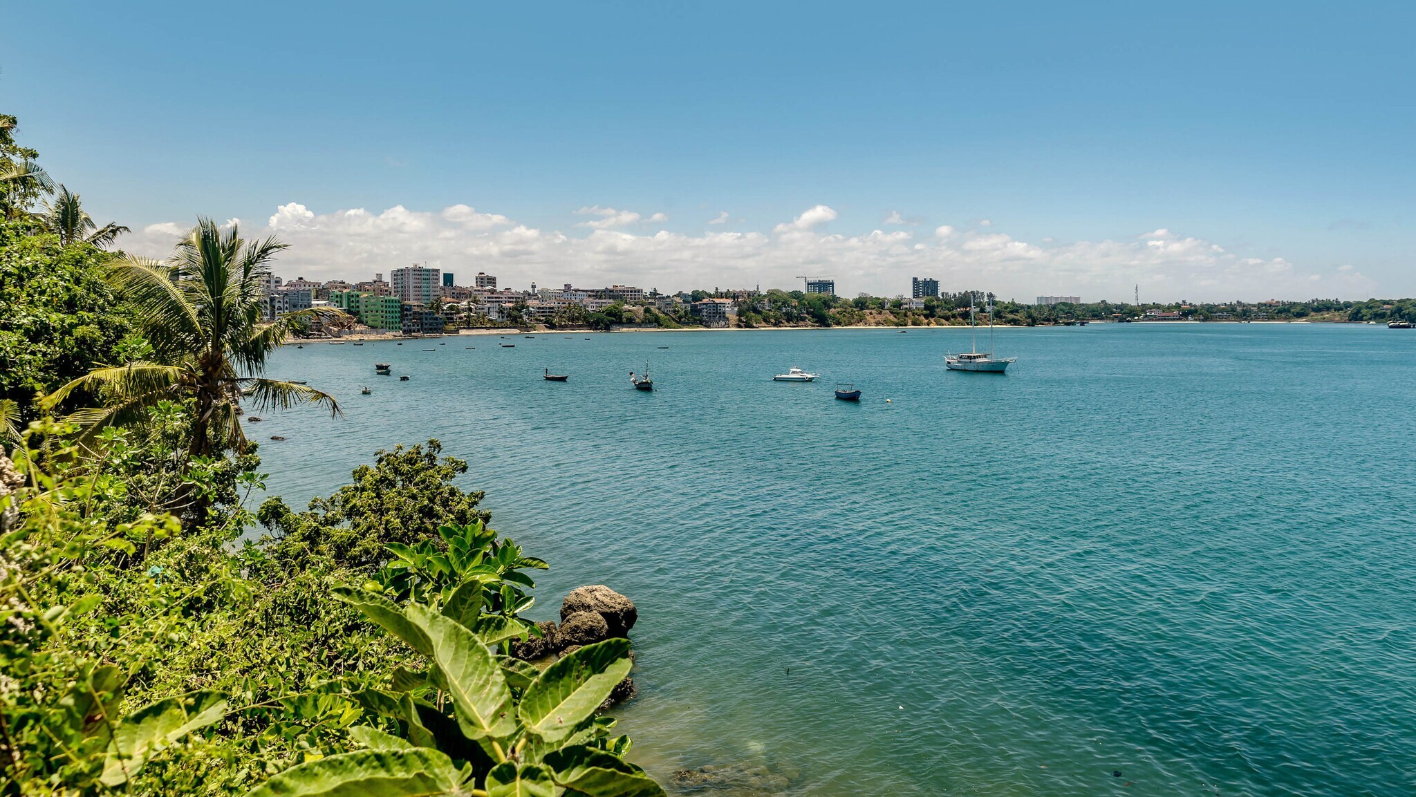 Küstenlinie mit grüner Vegetation und mehreren Booten auf ruhigem blauem Wasser unter bewölktem Himmel
