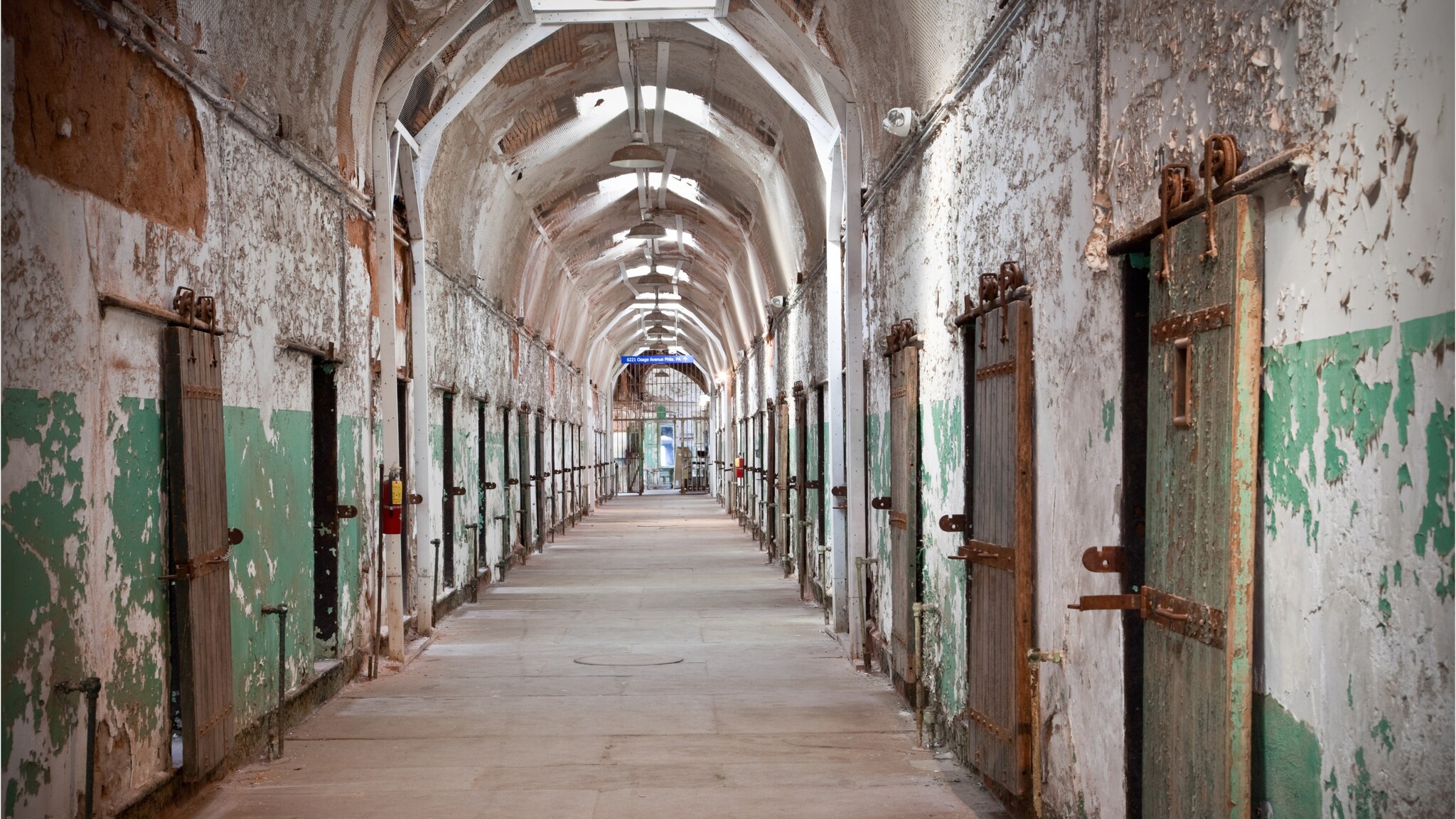 Langer, verfallener Gefängnisflur mit rostigen Metalltüren und bröckelnden Wänden unter gewölbter Decke