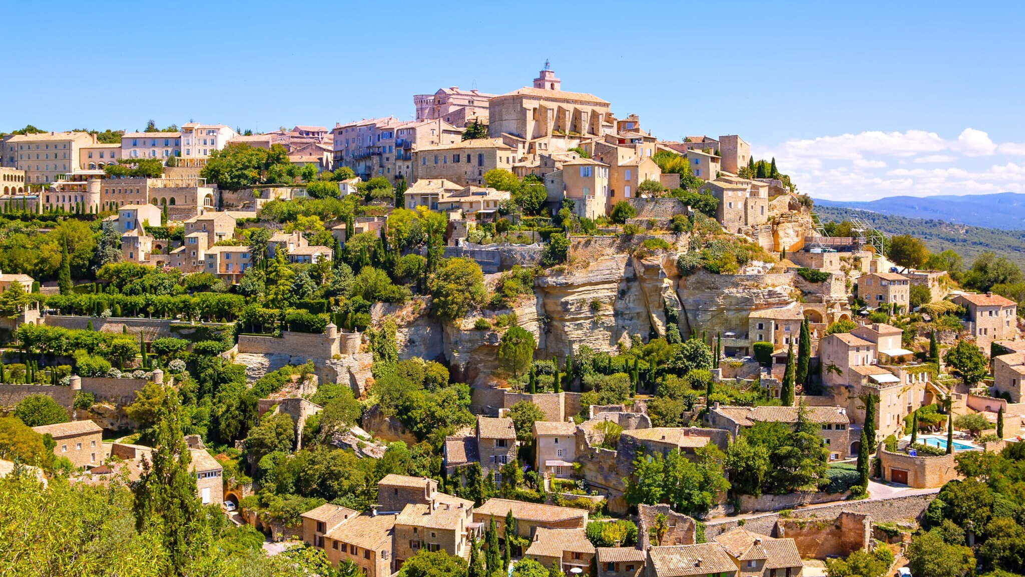 Historisches Dorf mit Steinhäusern und grünen Gärten auf einem Hügel unter blauem Himmel Historisches Dorf mit Steinhäusern und grünen Gärten auf einem Hügel unter blauem Himmel