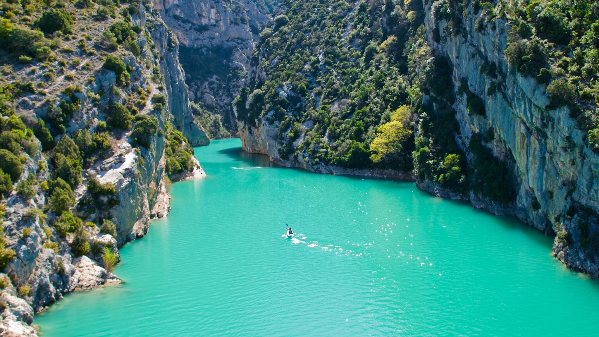 Türkisfarbener Fluss fließt durch enge, bewaldete Felsenschluchten unter klarem Himmel, eine Person paddelt im Kajak Türkisfarbener Fluss fließt durch enge, bewaldete Felsenschluchten unter klarem Himmel, eine Person paddelt im Kajak