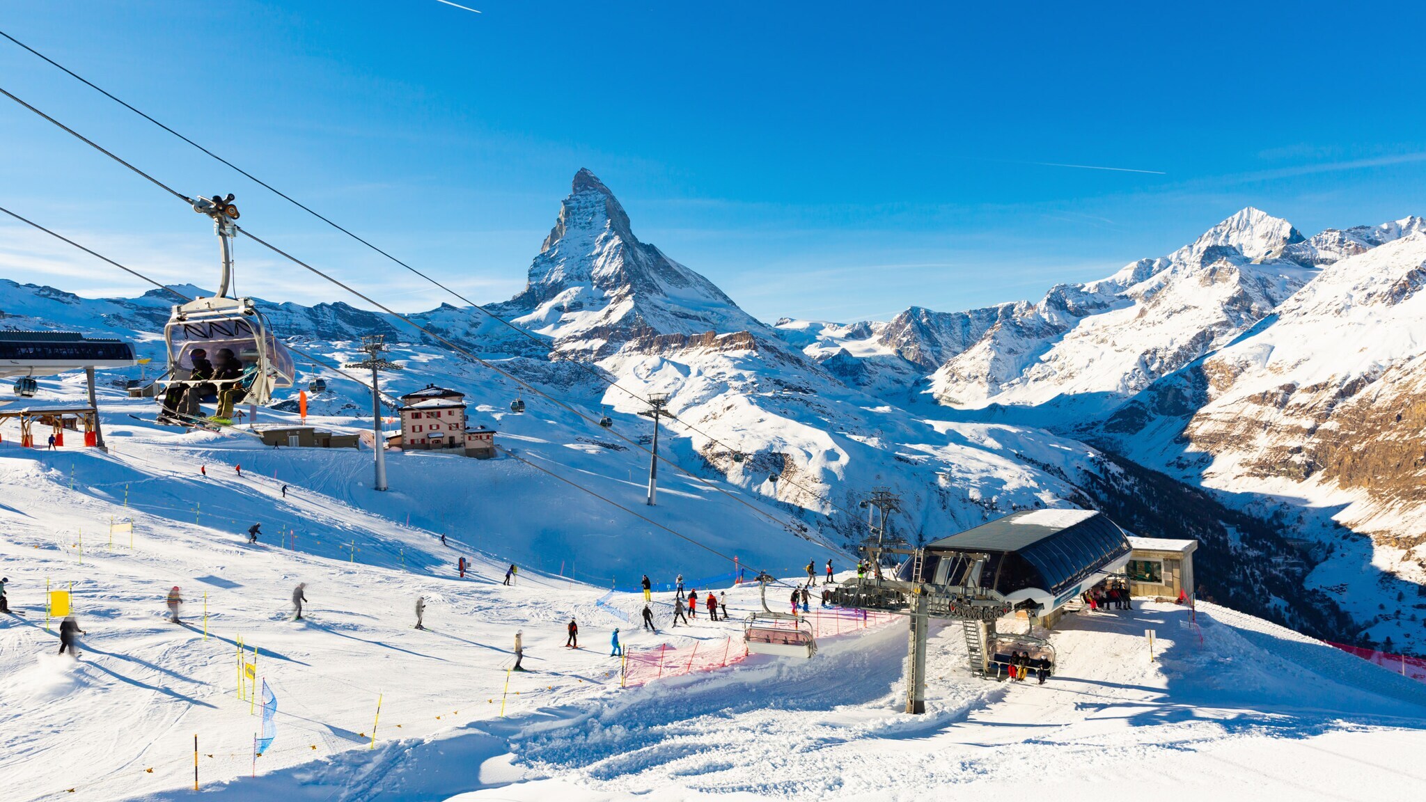 Skigebiet mit Seilbahn und Skifahrern vor schneebedecktem Matterhorn unter klarem blauem Himmel