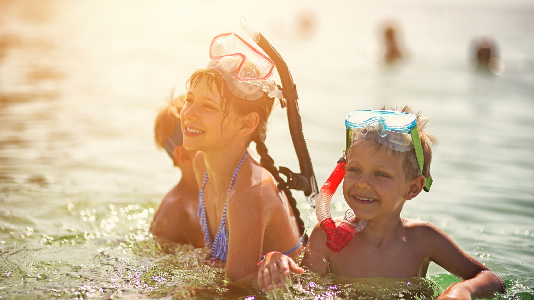 Lachende Kinder mit Schnorchelausrüstung spielen im Wasser bei Sonnenlicht Lachende Kinder mit Schnorchelausrüstung spielen im Wasser bei Sonnenlicht