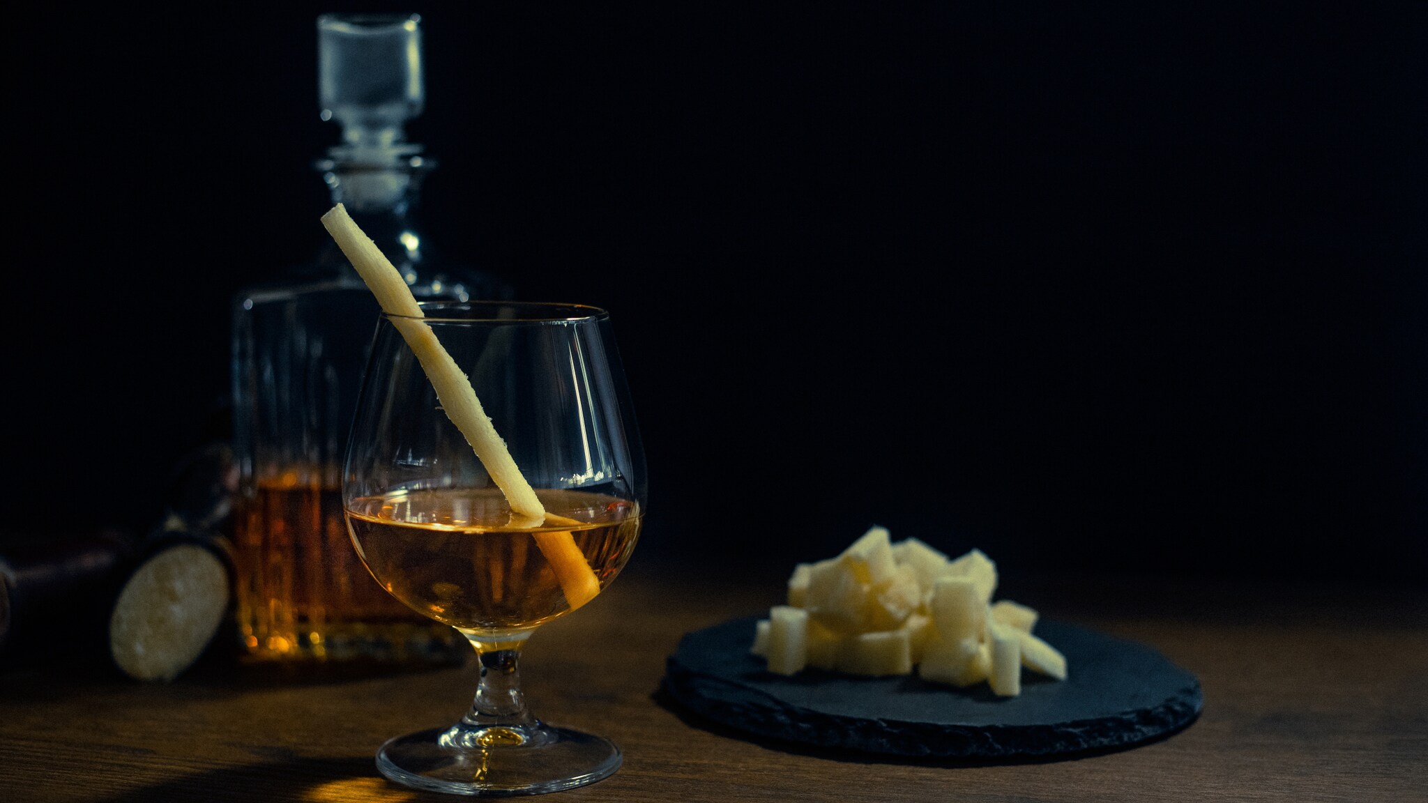 Glas mit braunem Getränk und Zuckerrohr, daneben ein Teller mit Zuckerrohr und eine Karaffe im Hintergrund Glas mit braunem Getränk und Zuckerrohr, daneben ein Teller mit Zuckerrohr und eine Karaffe im Hintergrund