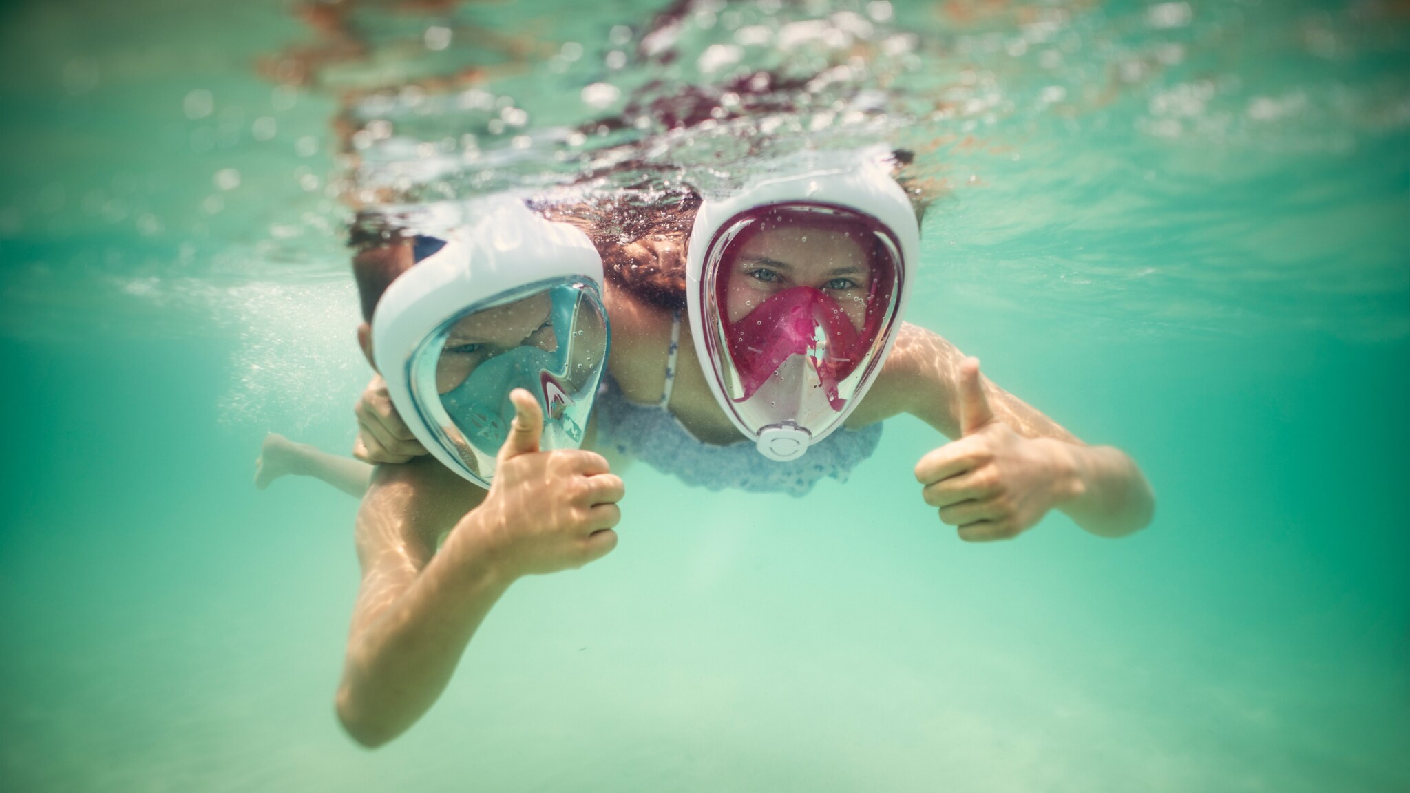 Zwei Kinder mit Vollgesichtsschnorchelmasken tauchen unter Wasser und zeigen Daumen hoch Zwei Kinder mit Vollgesichtsschnorchelmasken tauchen unter Wasser und zeigen Daumen hoch