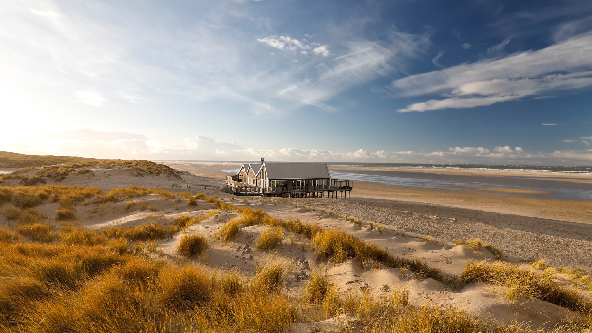 Haus auf Stelzen am Strand mit Dünen und weiter Meeresküste unter blauem Himmel. Haus auf Stelzen am Strand mit Dünen und weiter Meeresküste unter blauem Himmel.