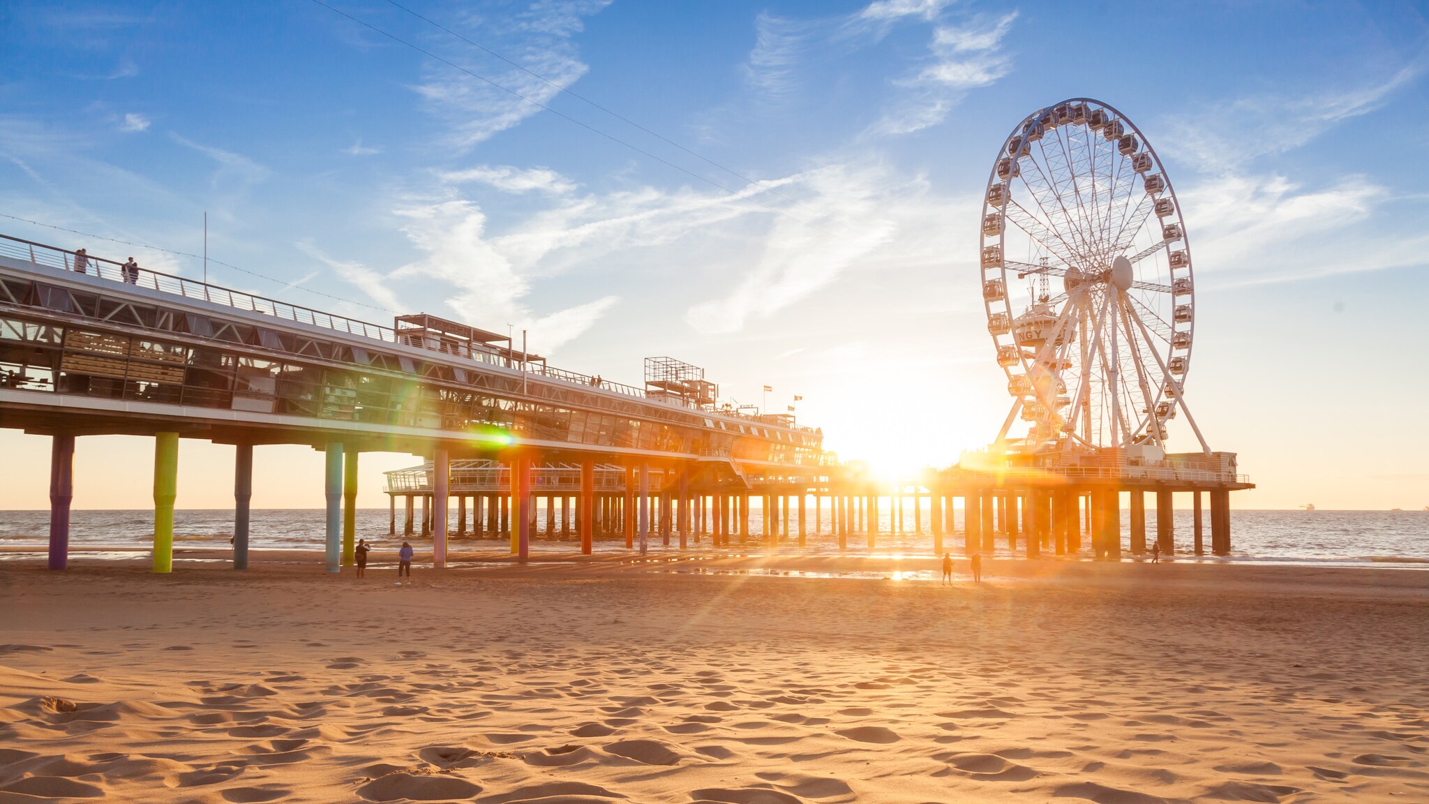 Sonnenuntergang am Strand mit einem Pier und einem großen Riesenrad am Meer.