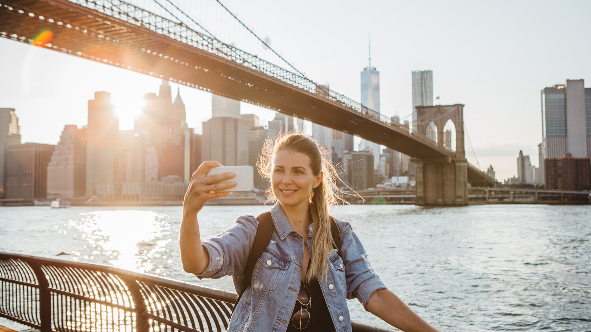 Frau macht Selfie vor der Brooklyn Bridge und der Skyline von New York bei Sonnenuntergang Frau macht Selfie vor der Brooklyn Bridge und der Skyline von New York bei Sonnenuntergang