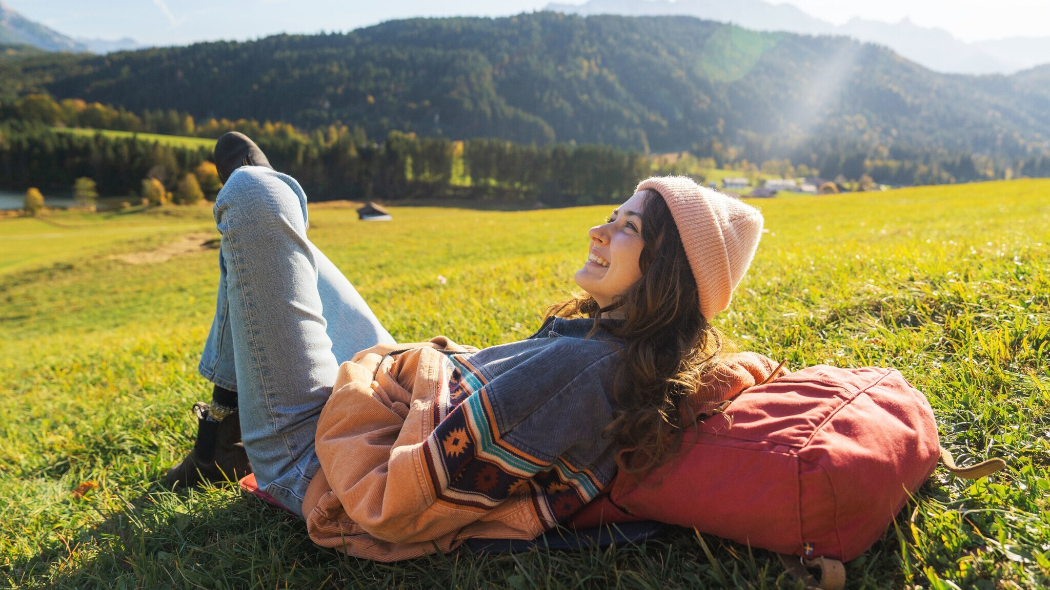 Eine Frau ruht sich auf einer Wiese in der Sonne aus, dabei liegt sie auf ihrem Wanderrucksack. Eine Frau ruht sich auf einer Wiese in der Sonne aus, dabei liegt sie auf ihrem Wanderrucksack.