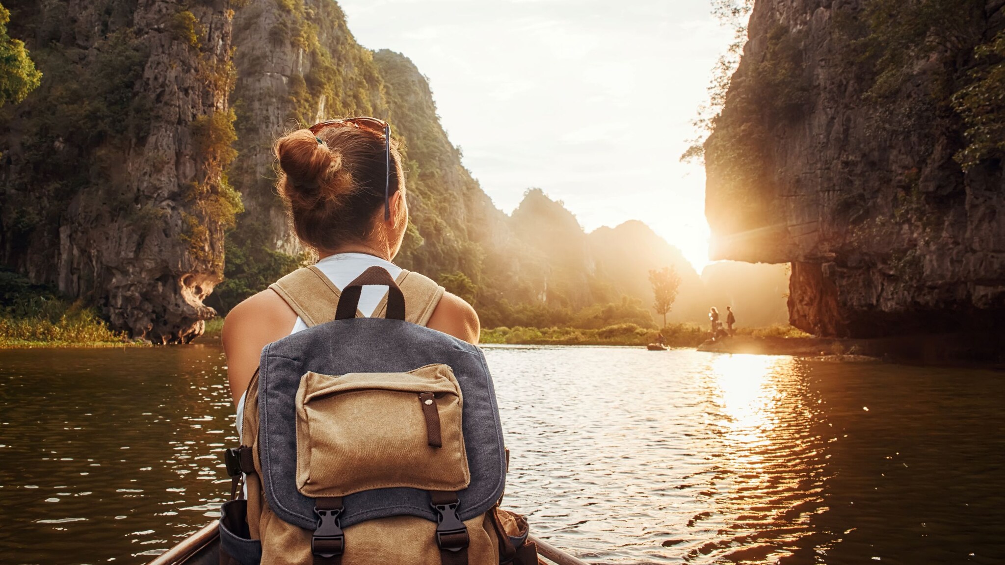 Frau mit Rucksack sitzt in einem Kanu auf einem Fluss, umgeben von hohen Felsen bei Sonnenuntergang.