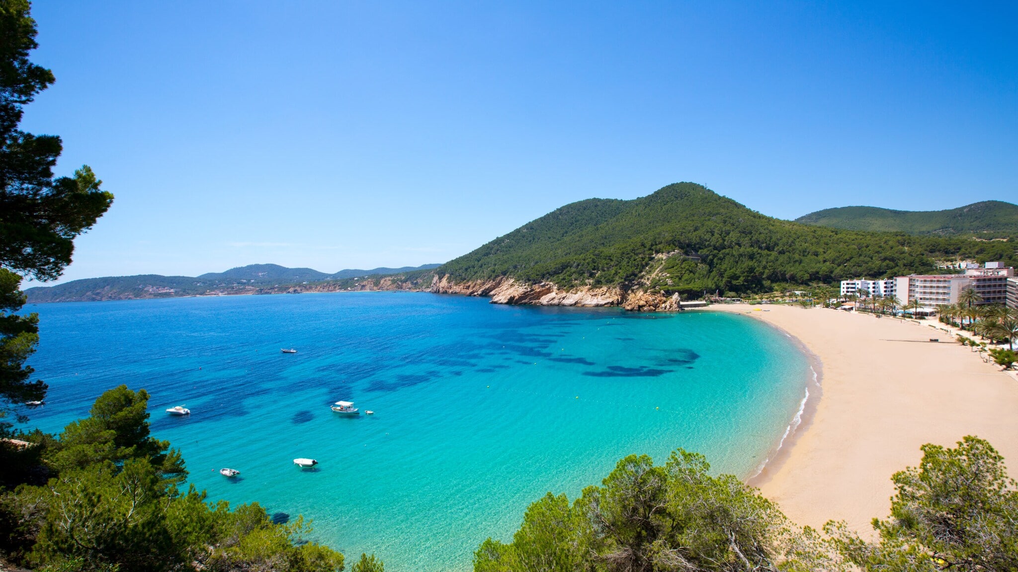 Bucht mit türkisfarbenem Wasser, Sandstrand und bewaldeten Hügeln unter klarem Himmel Bucht mit türkisfarbenem Wasser, Sandstrand und bewaldeten Hügeln unter klarem Himmel