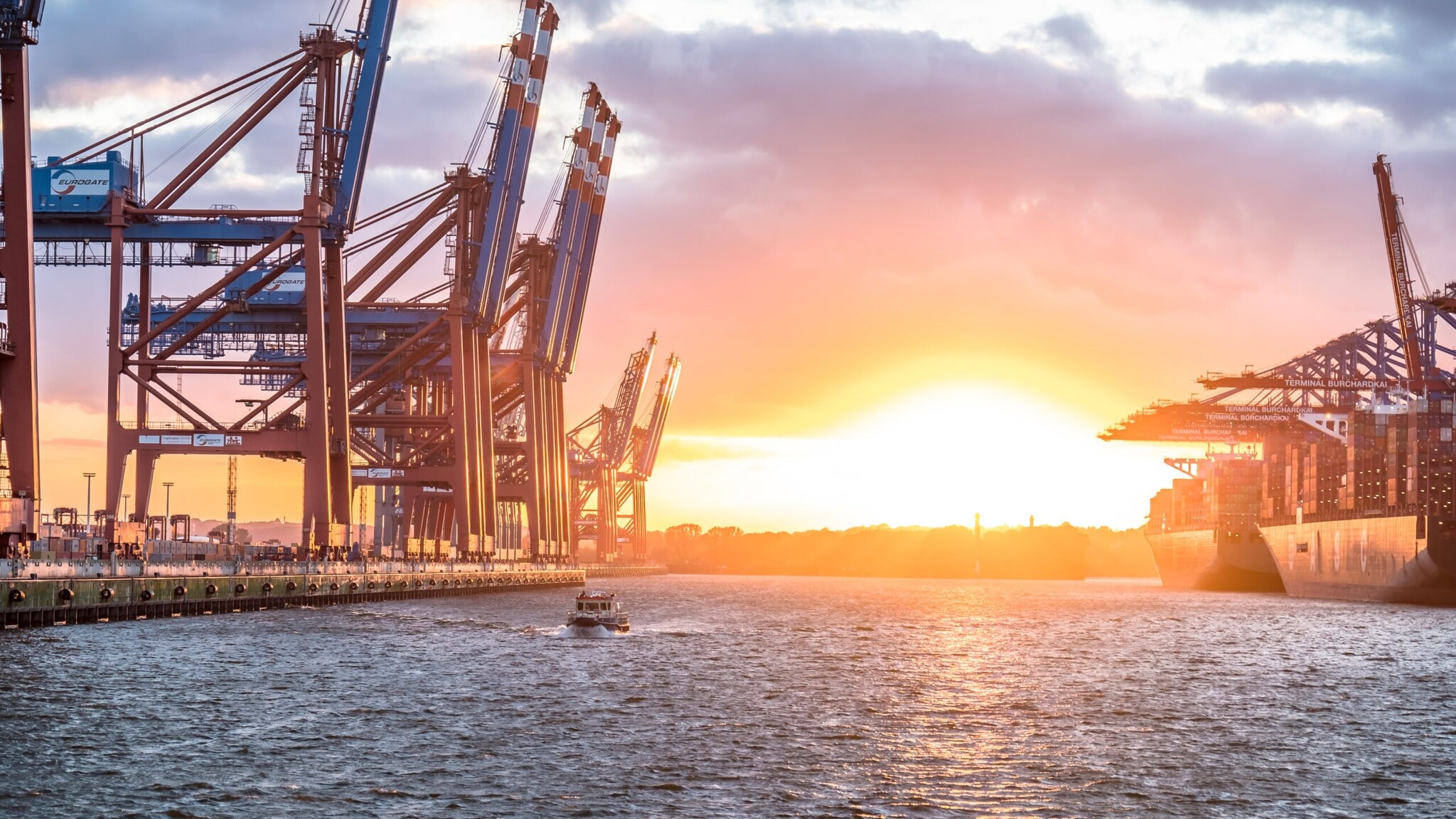 Sonnenuntergang über dem Waltershofer Hafen mit großen Containerkränen und einem Schiff im Wasser. Sonnenuntergang über dem Waltershofer Hafen mit großen Containerkränen und einem Schiff im Wasser.