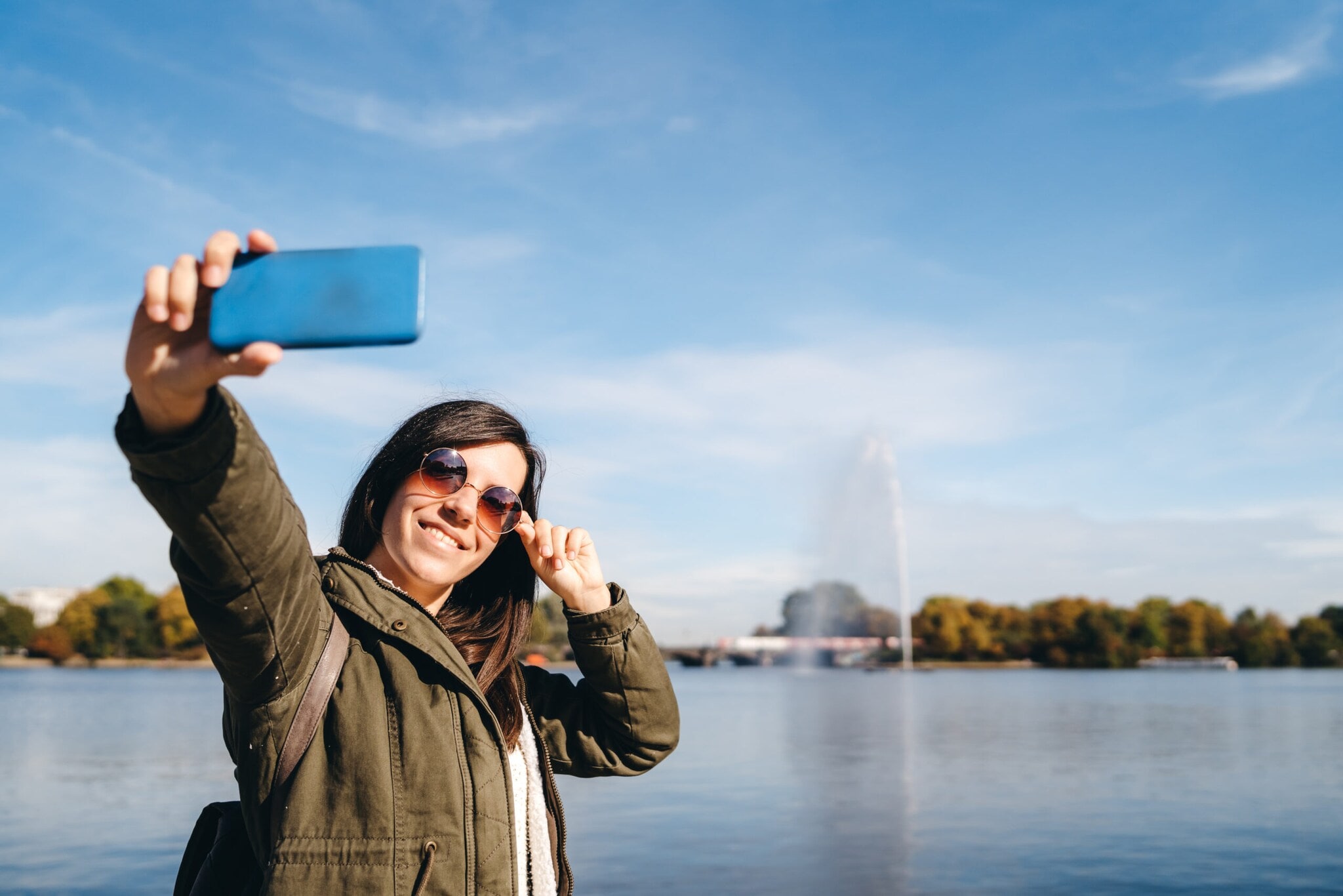 Eine Frau macht ein Selfie mit der Fontäne der Binnenalster im Hintergrund. Eine Frau macht ein Selfie mit der Fontäne der Binnenalster im Hintergrund.