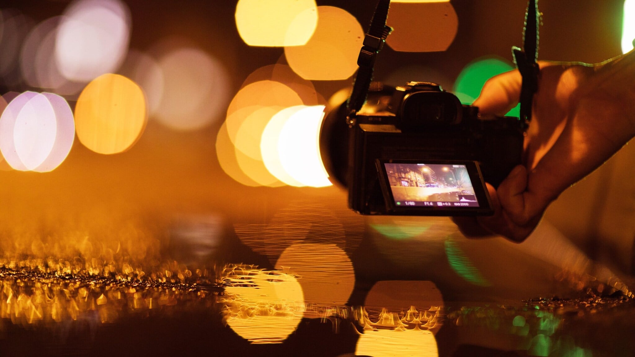 Digitalkamera mit Display, das eine nächtliche Straßenszene mit Lichtern zeigt, vor unscharfem Hintergrund mit orangefarbenen Lichtpunkten Digitalkamera mit Display, das eine nächtliche Straßenszene mit Lichtern zeigt, vor unscharfem Hintergrund mit orangefarbenen Lichtpunkten