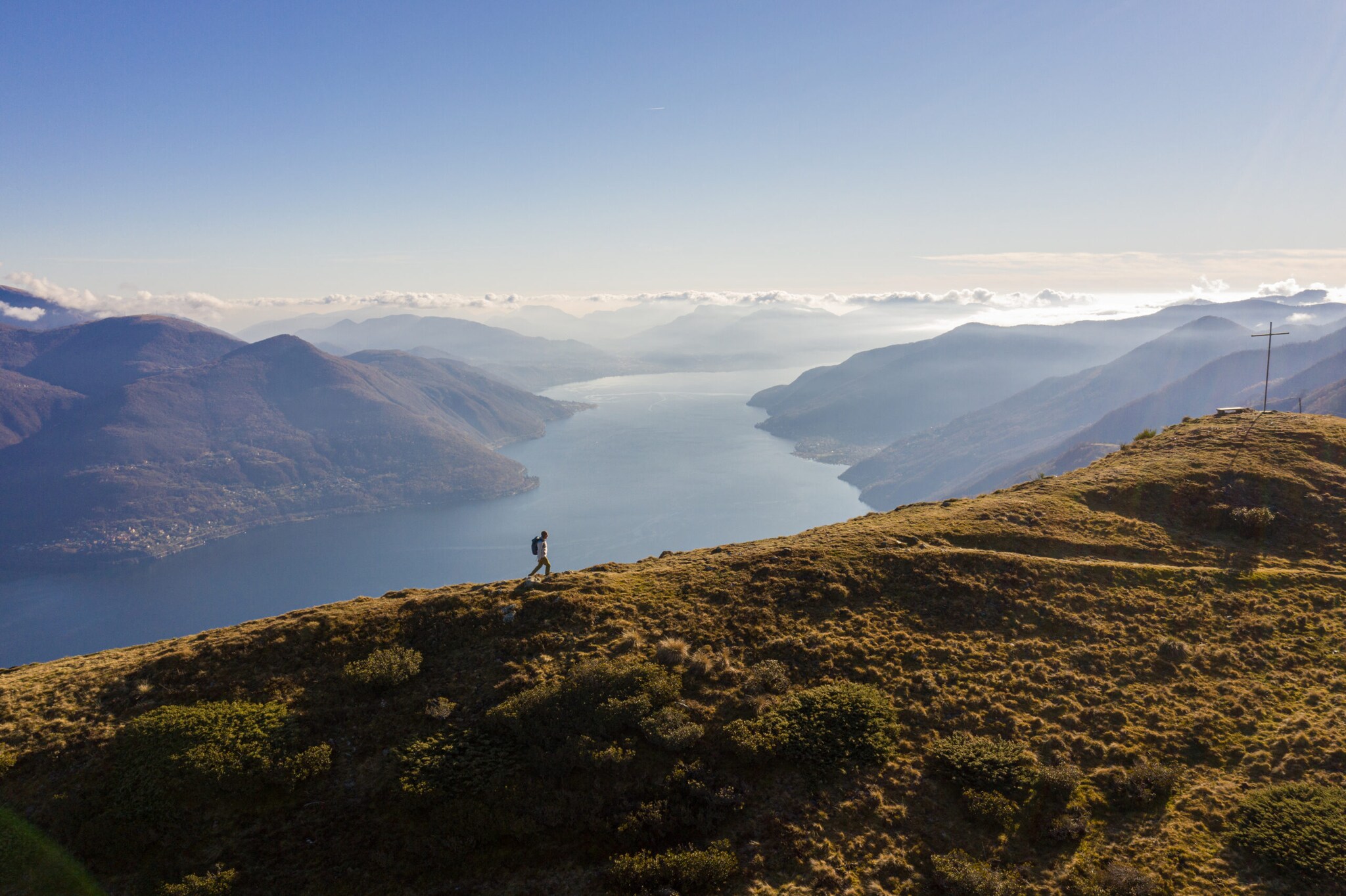 Panoramaaufnahme von einem Mann mit Rucksack auf einem Berg und dem Lago Maggiore im Hintergrund.