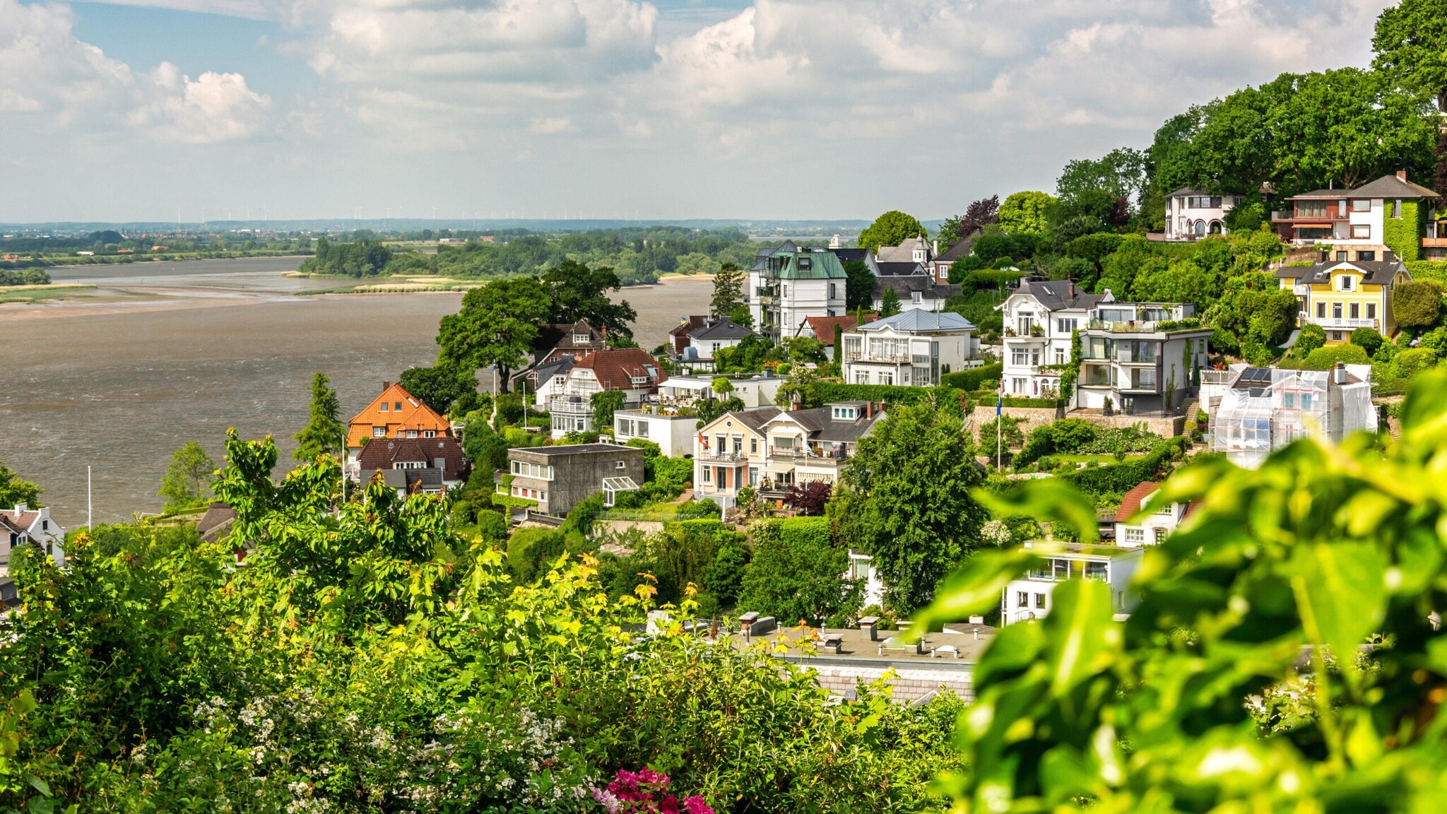Blick auf ein grünes Wohngebiet mit Villen am Flussufer unter bewölktem Himmel. Blick auf ein grünes Wohngebiet mit Villen am Flussufer unter bewölktem Himmel.