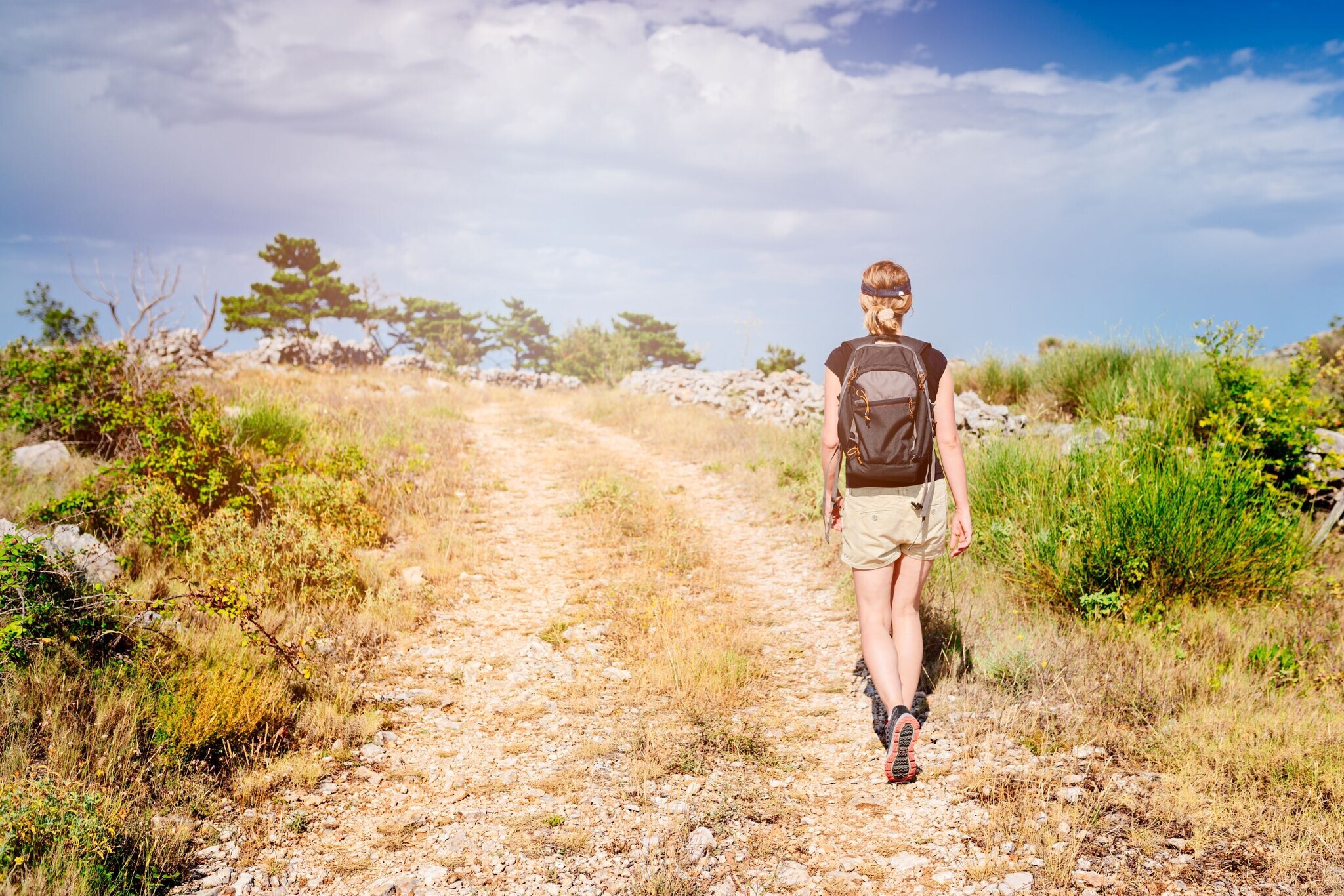 Rückansicht einer Person mit Rucksack auf einem Wanderweg bei sonnigem Wetter. Rückansicht einer Person mit Rucksack auf einem Wanderweg bei sonnigem Wetter.