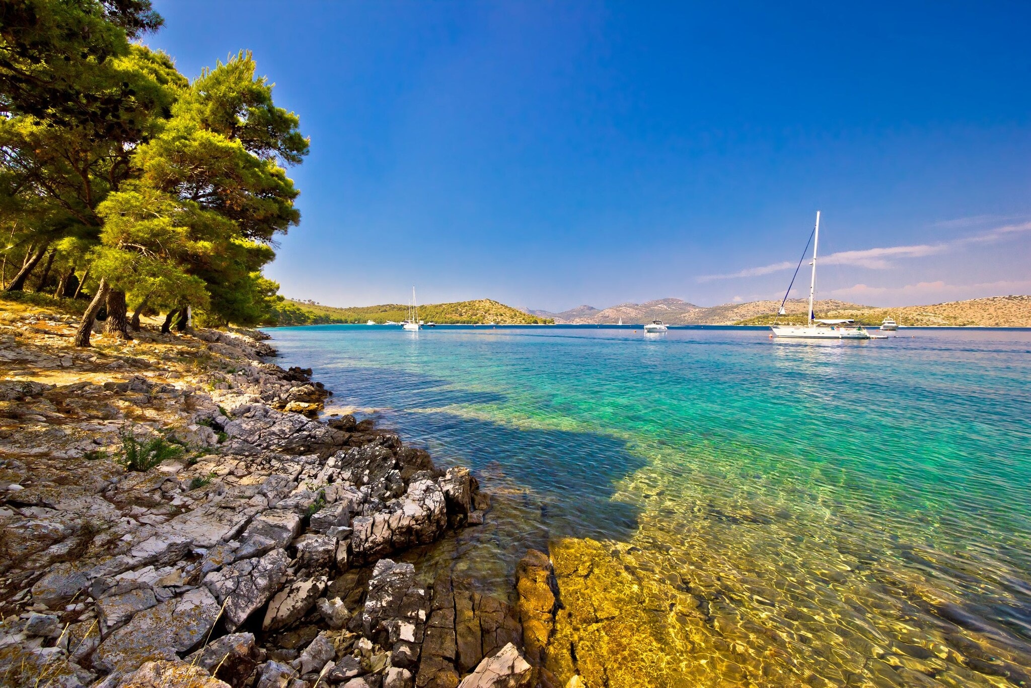 Bucht mit klarem Wasser und Booten umgeben von einer felsigen Landschaft mit Bäumen. Bucht mit klarem Wasser und Booten umgeben von einer felsigen Landschaft mit Bäumen.