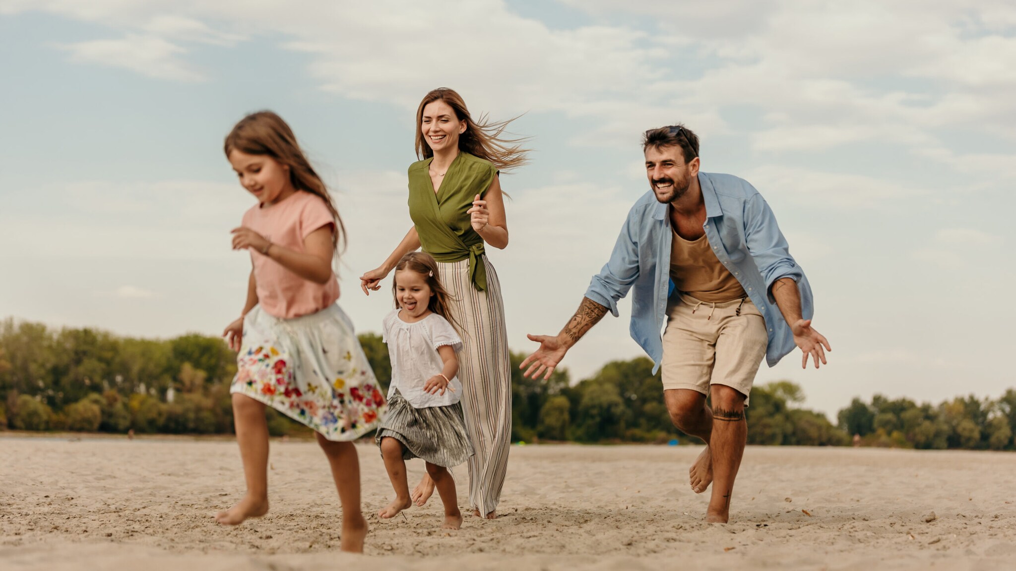 Familie mit zwei Kindern läuft barfuß am Strand bei bewölktem Himmel