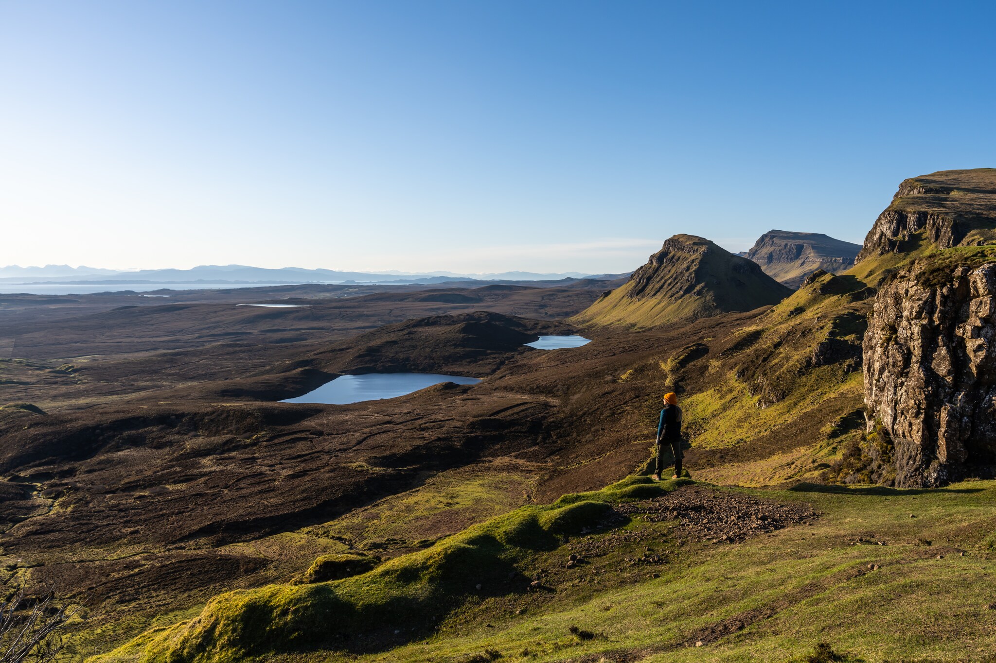 Eine Person steht in einer Landschaft aus Wiesen, Hügeln und Seen in Schottland.