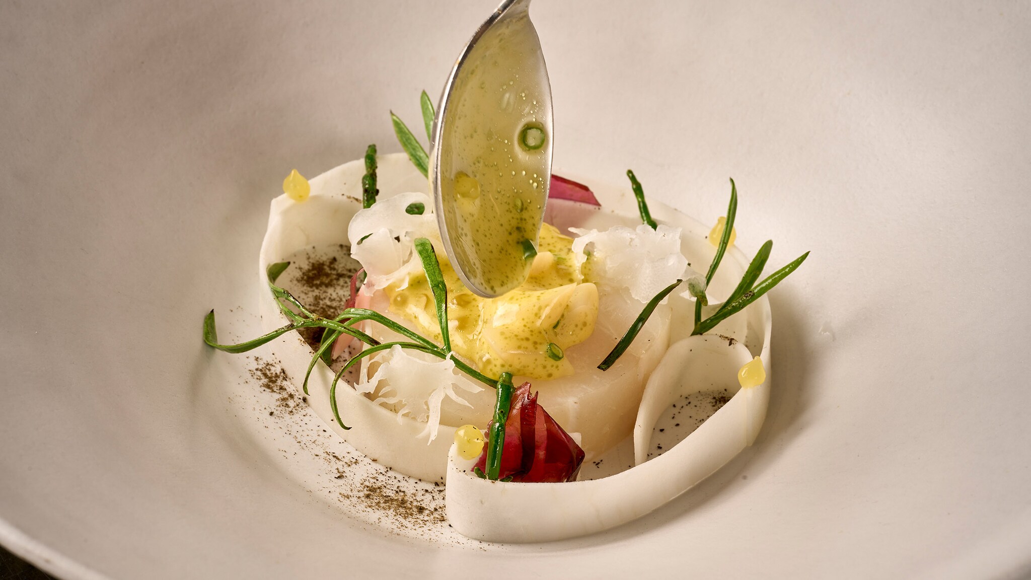 amex-magazin-berlin-sternerestaurants-rutz Ein stilvoll angerichtetes Fischgericht mit heller Soße auf einem weißen Teller.