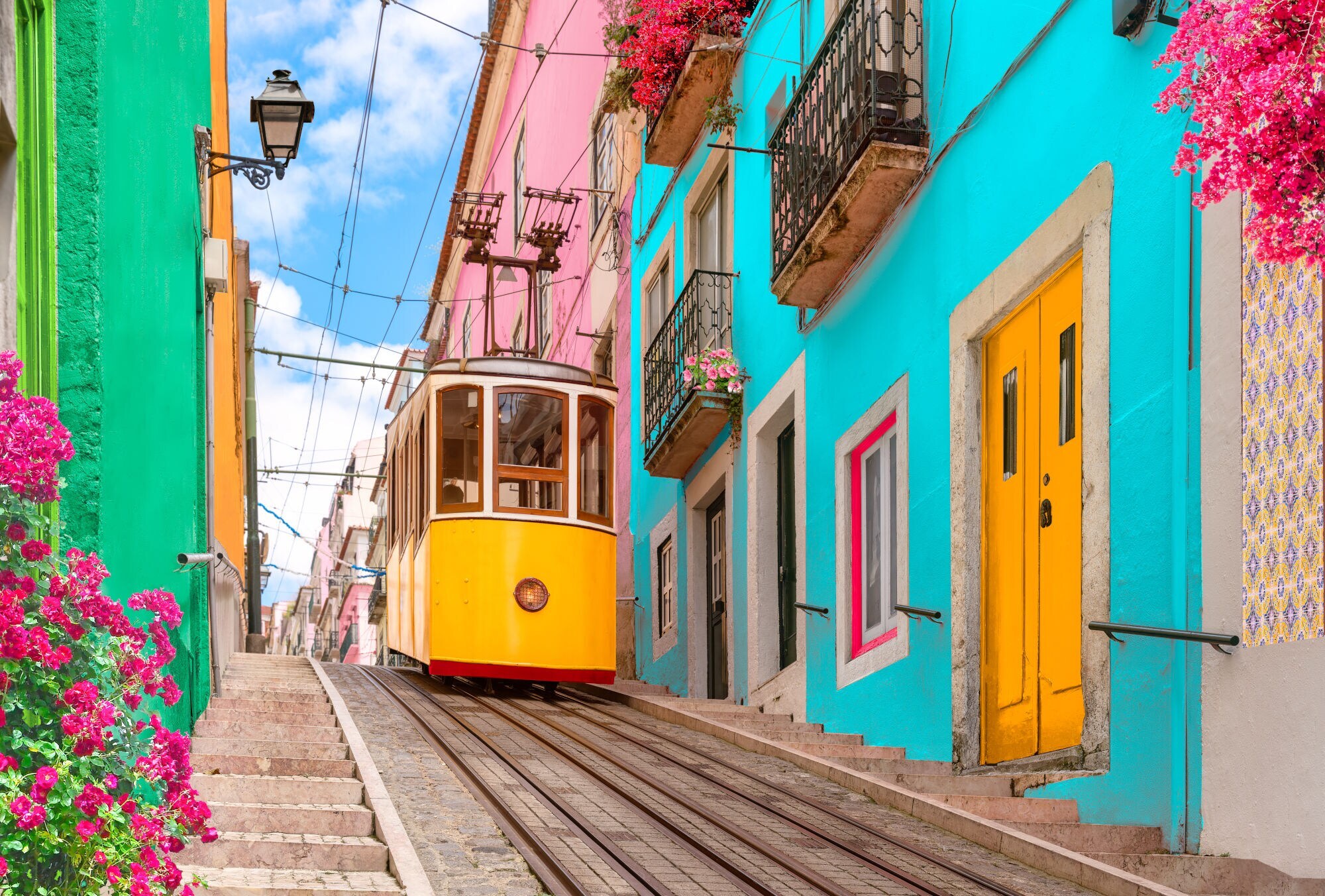 Typische gelbe Straßenbahn in Lissabon, die an bunten Häusern und bepflanzten Balkonen vorbeifährt. Typische gelbe Straßenbahn in Lissabon, die an bunten Häusern und bepflanzten Balkonen vorbeifährt.