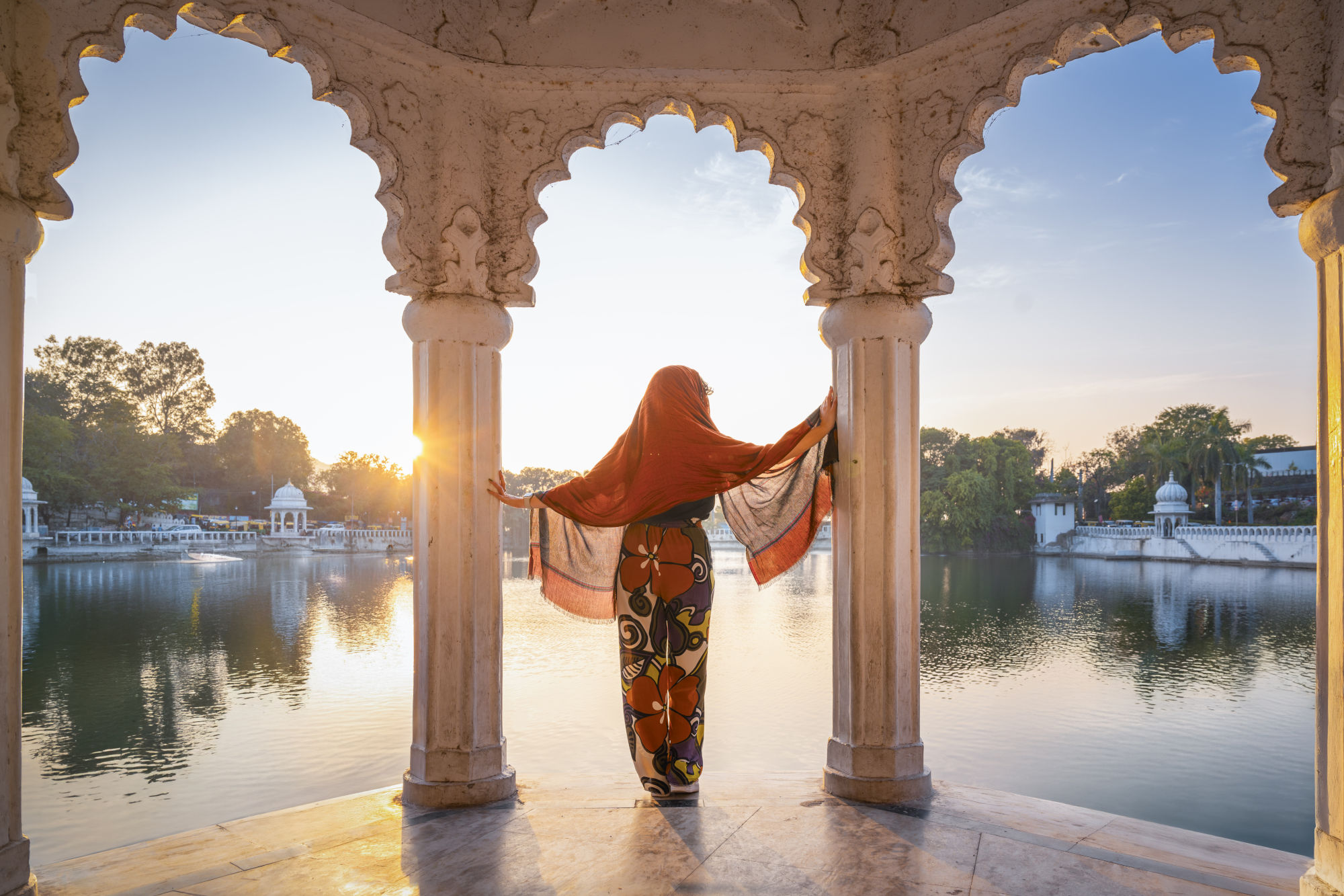 Eine Frau in traditioneller indischer Kleidung steht in einem Pavillon und blickt aufs Wasser.