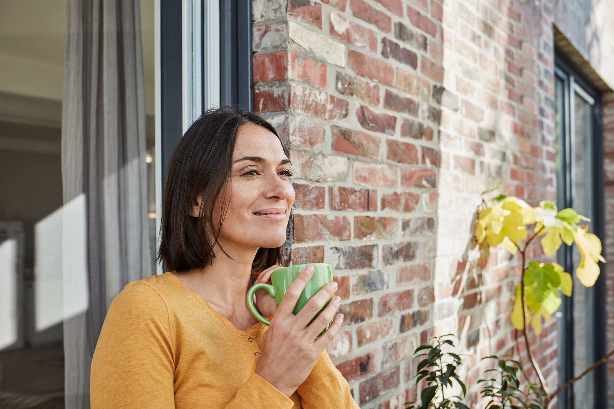 Therapeutic Laziness: Pausen statt Powern Eine Frau mit einer Tasse in der Hand lehnt entspannt an der Hauswand.