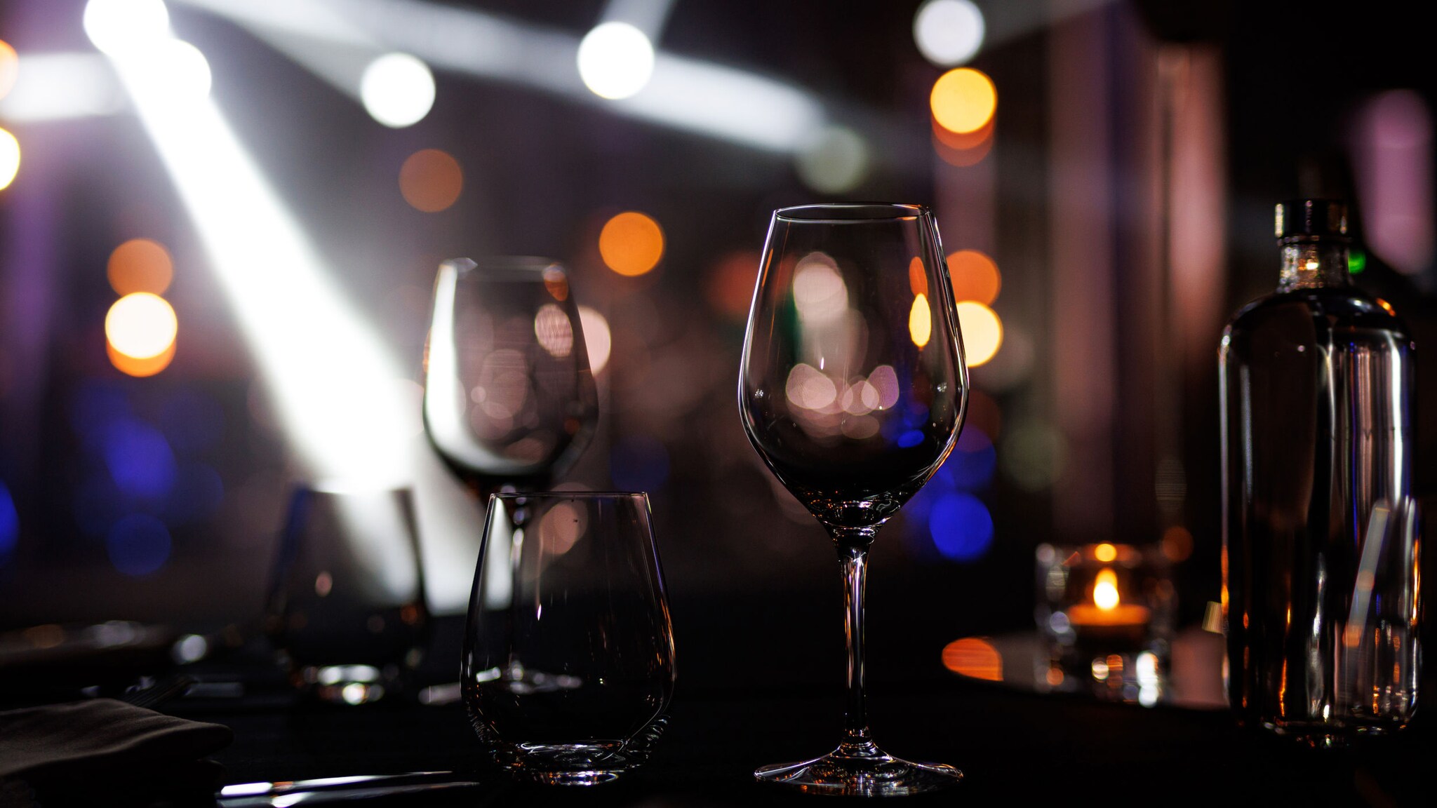 Leere Weingläser und eine Flasche auf einem Tisch vor unscharfem Hintergrund mit Lichtern