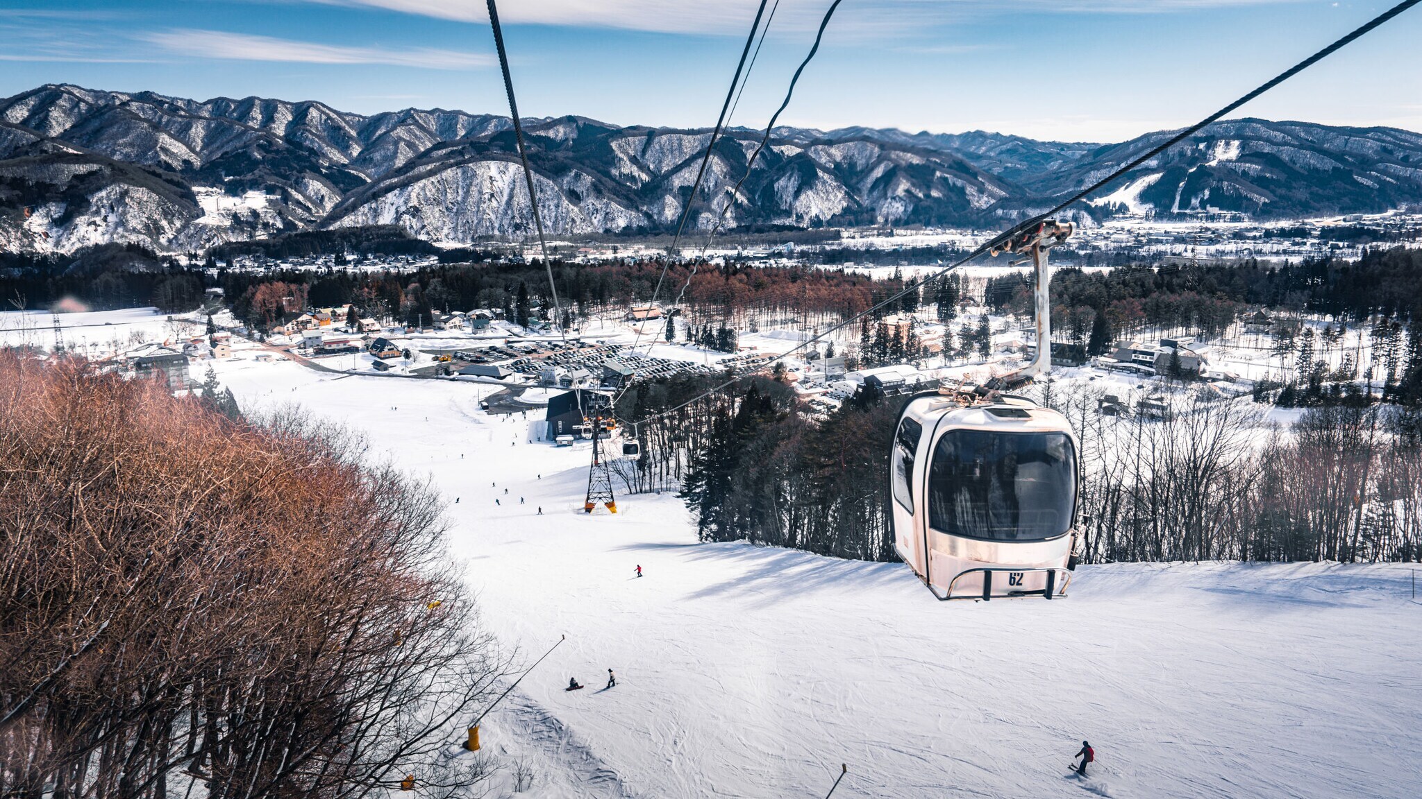 Blick von einem Sessellift auf ein schneebedecktes Skigebiet mit Skifahrern und Bergen im Hintergrund